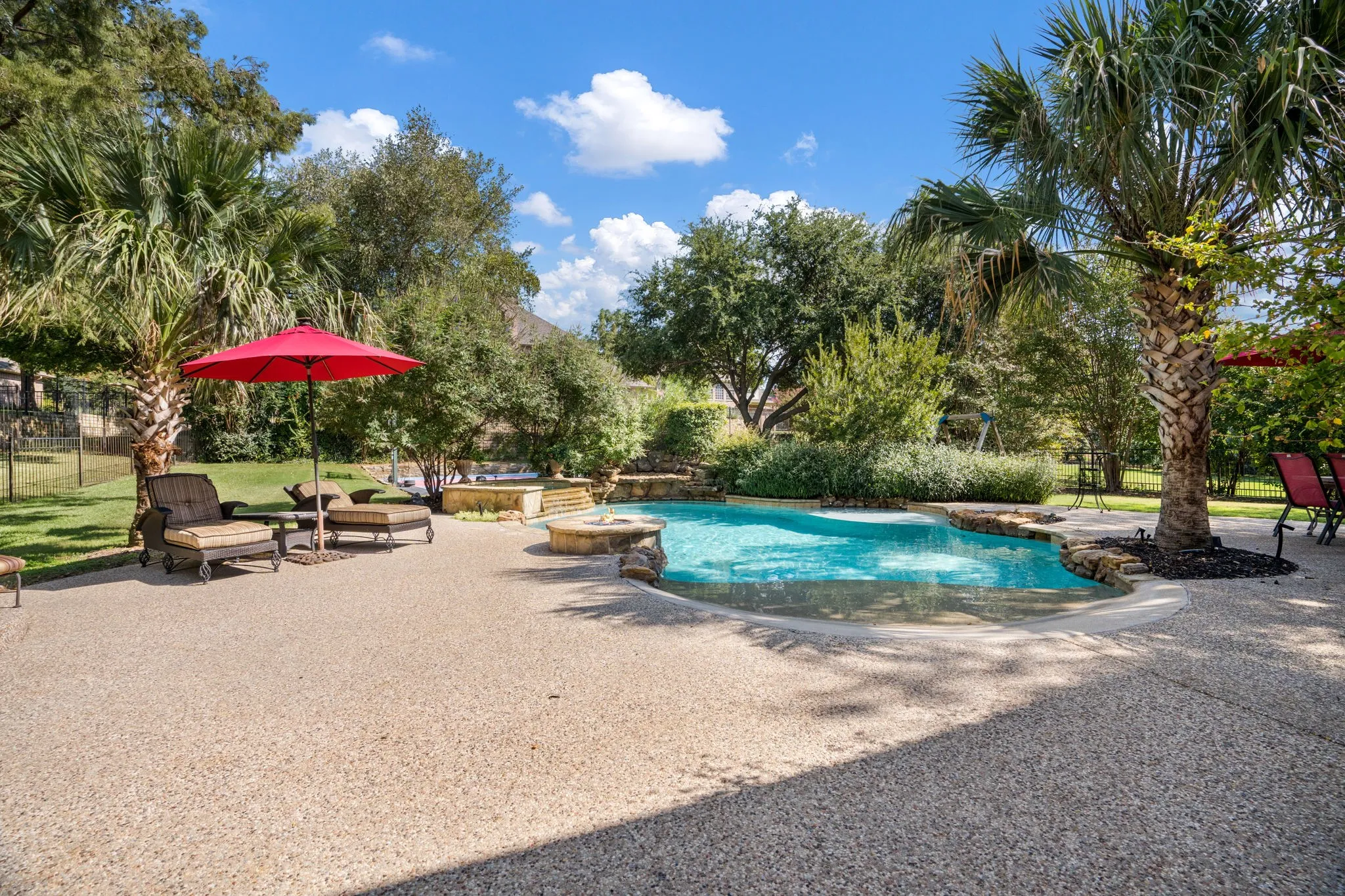 Expansive outdoor living area featuring a sparkling pool, surrounding stone hardscaping, and mature landscaping