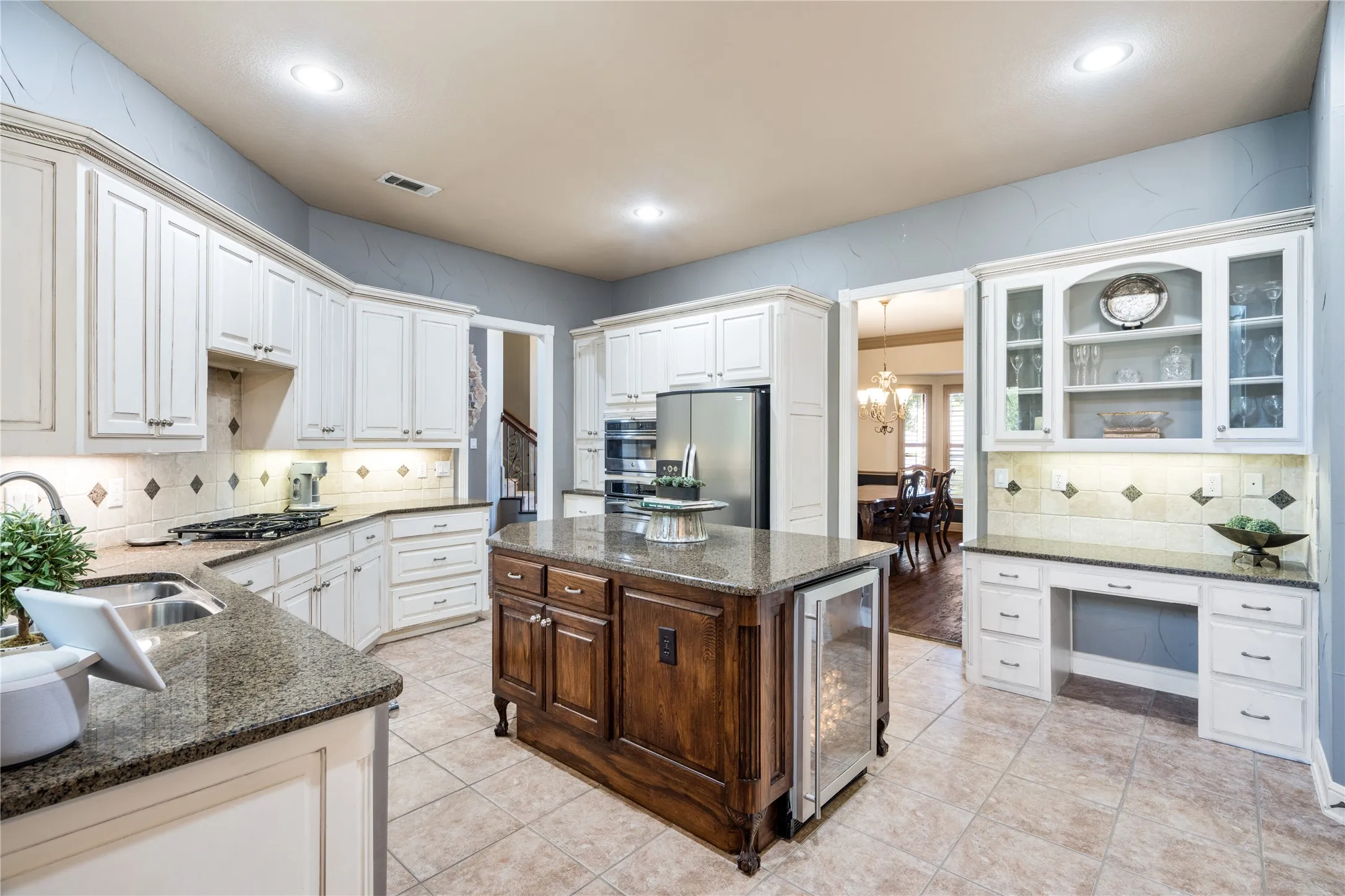 Expansive kitchen featuring white cabinetry, stone countertops, a large island with a built-in beverage cooler, stainless steel appliances, and tile flooring