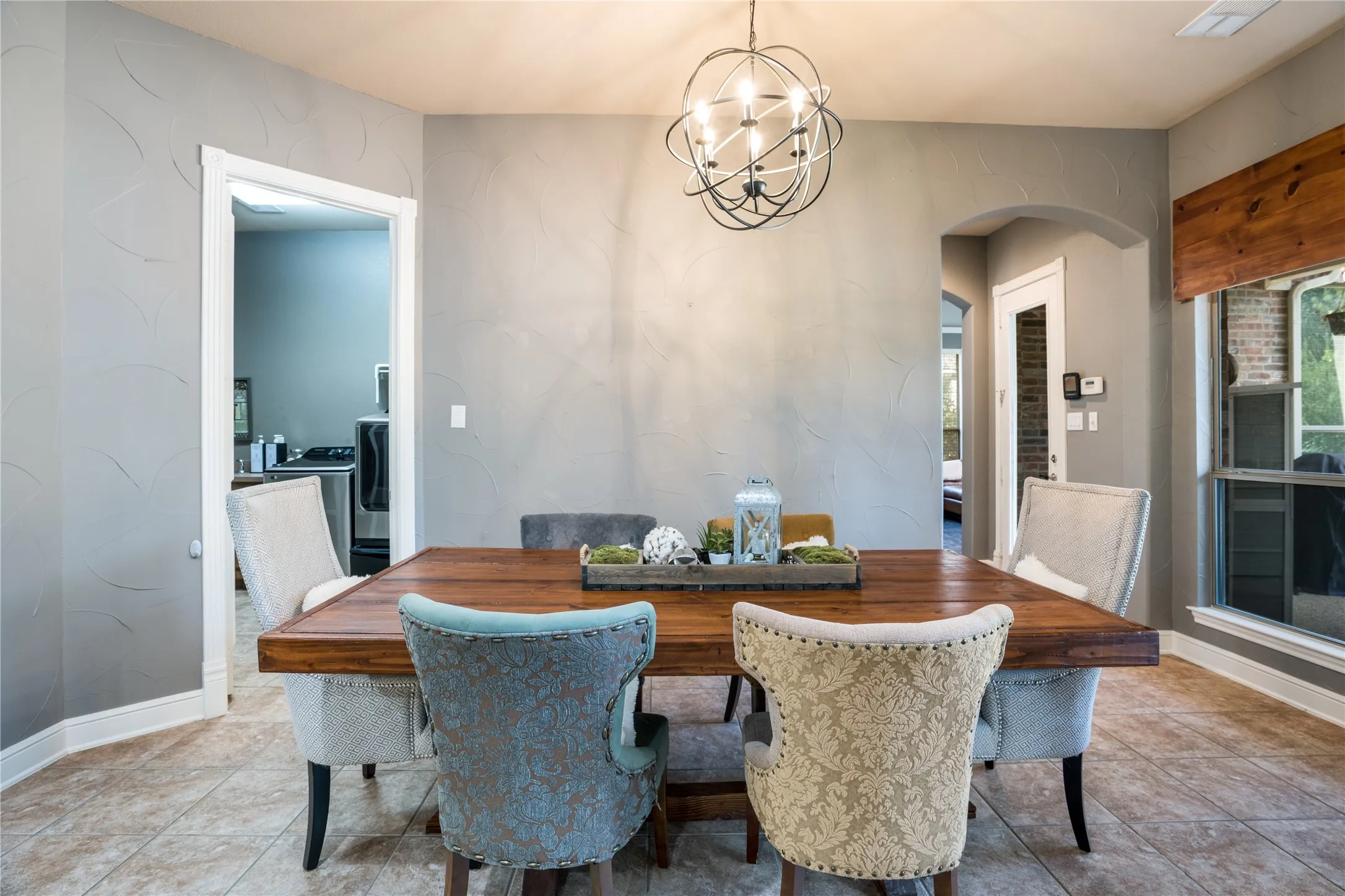 Dining area featuring a wood-finish table, tile flooring, a spherical chandelier, and an arched doorway