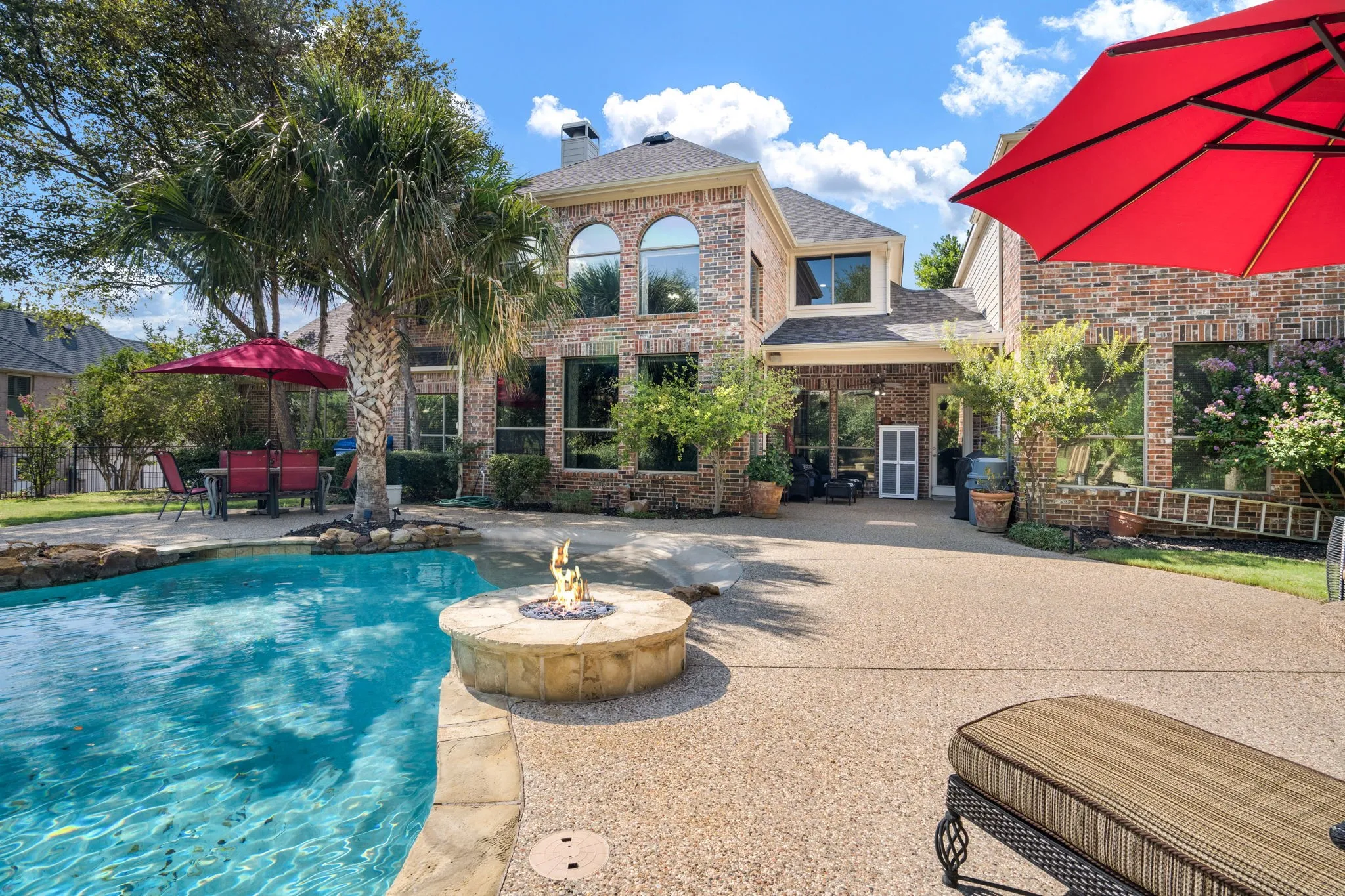 Brick exterior with arched windows, expansive pool, integrated fire pit, and mature palm trees