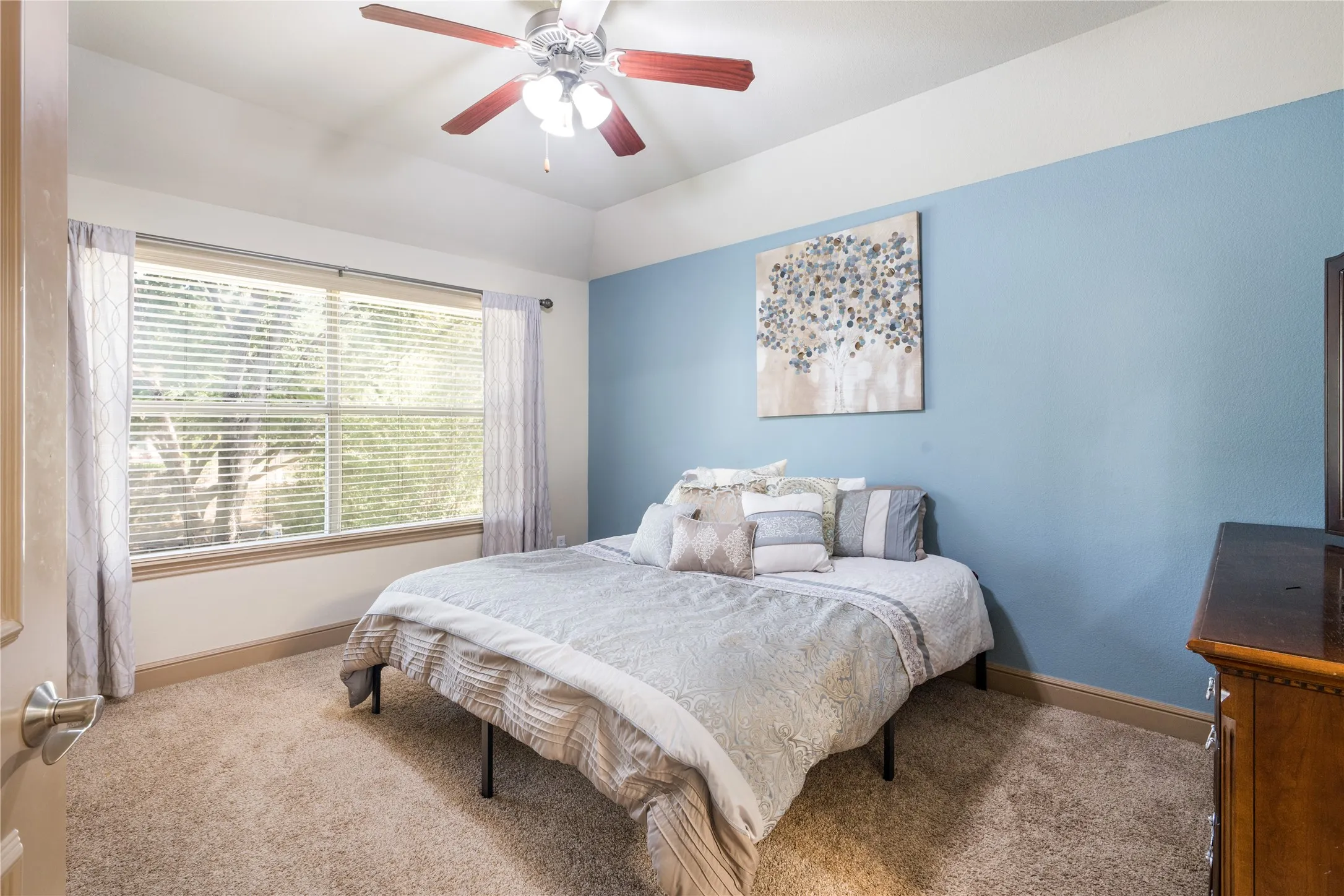 Recessed ceiling with a ceiling fan, broad window with blinds, carpeted flooring, and a painted accent wall