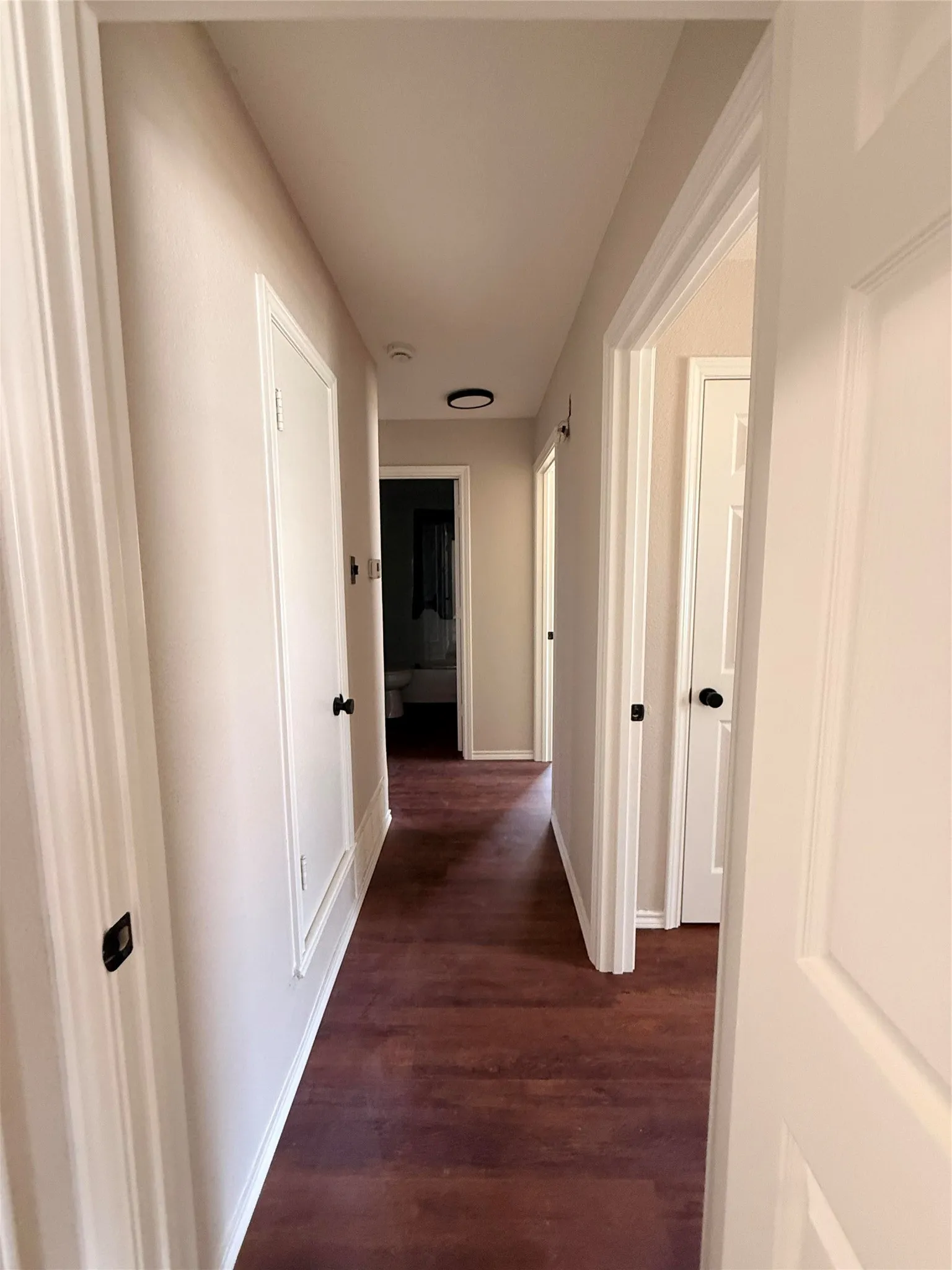 Hallway featuring wood-finish flooring, light-toned wall paint, white trim, and doors with black hardware
