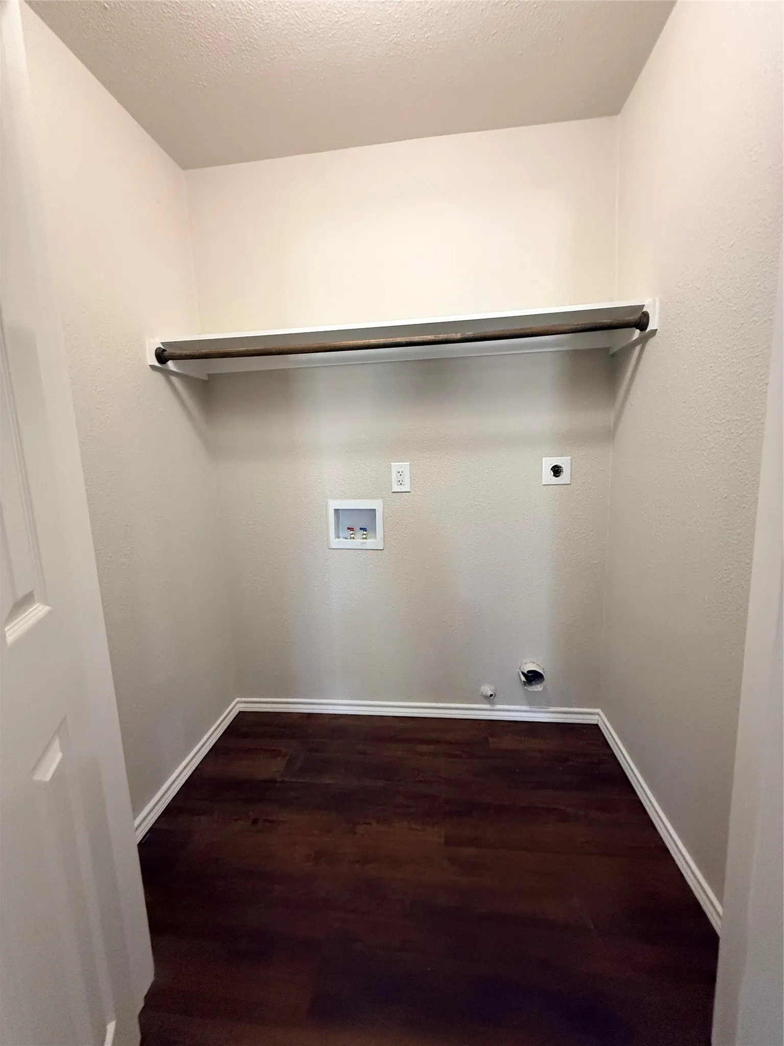 Laundry area featuring wood-finish flooring, light-toned walls, and a built-in shelf with a hanging rod