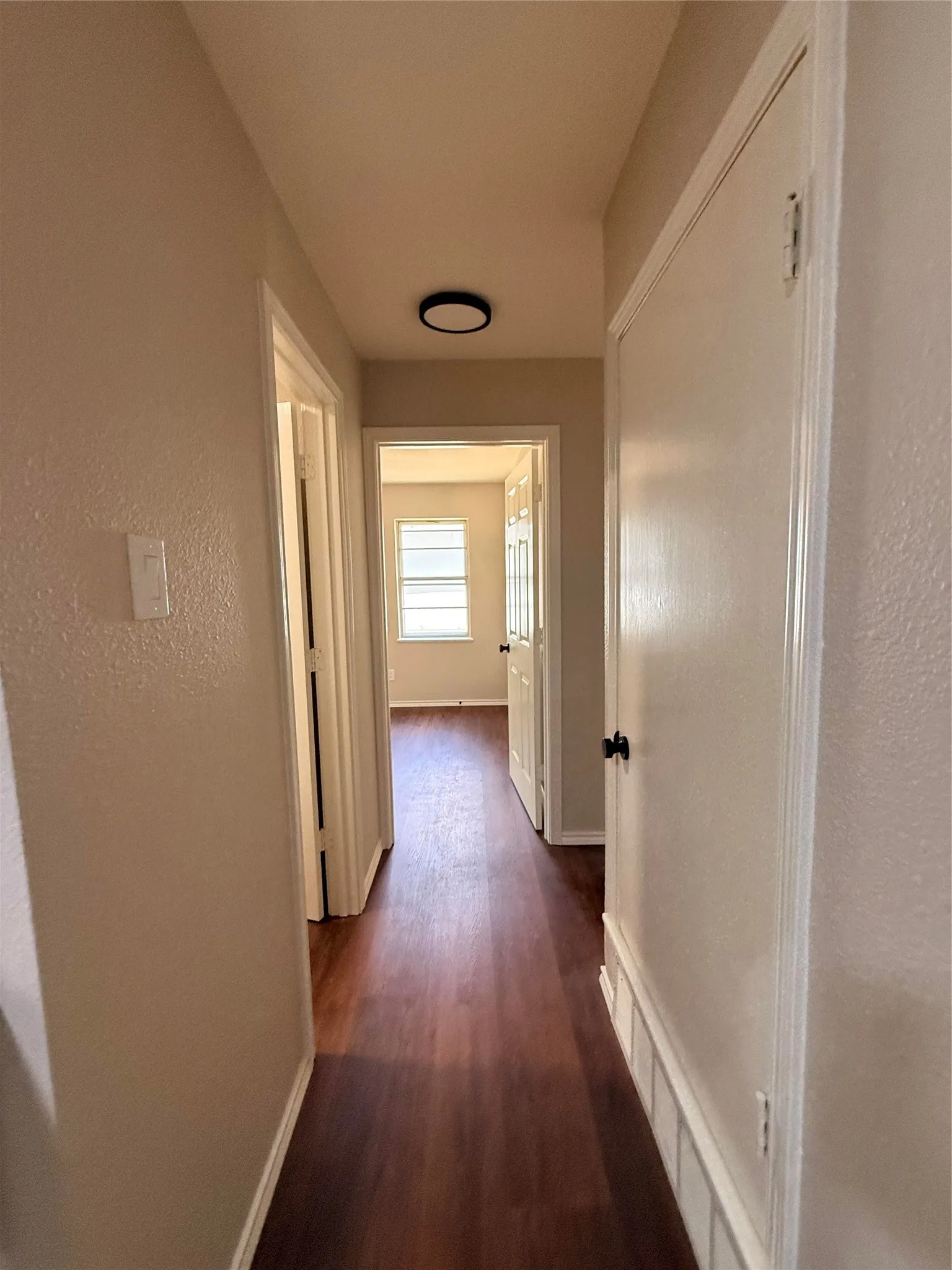 Hallway featuring wood-finish flooring, light-toned walls, and a contemporary flush-mount ceiling light