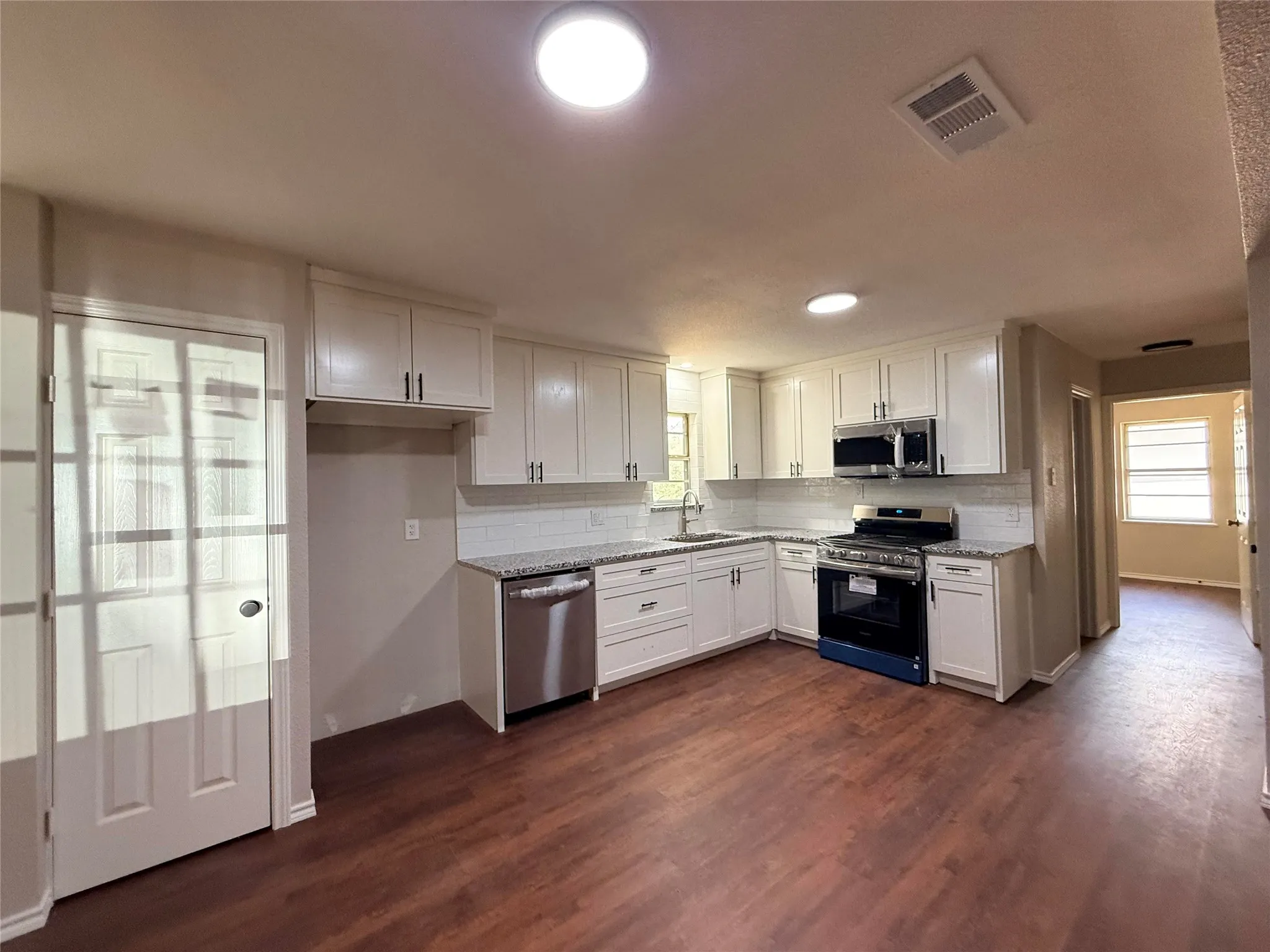 Kitchen featuring wood-finish flooring, white cabinetry, granite countertops, a subway tile backsplash, and stainless steel appliances