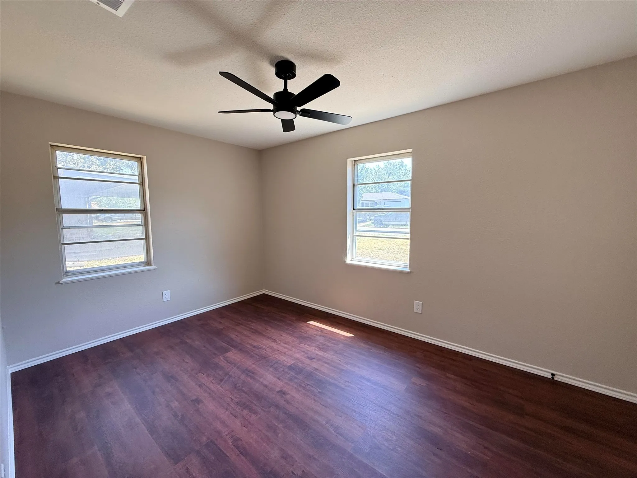 Spacious room featuring wood-finish flooring, two windows, and a ceiling fan