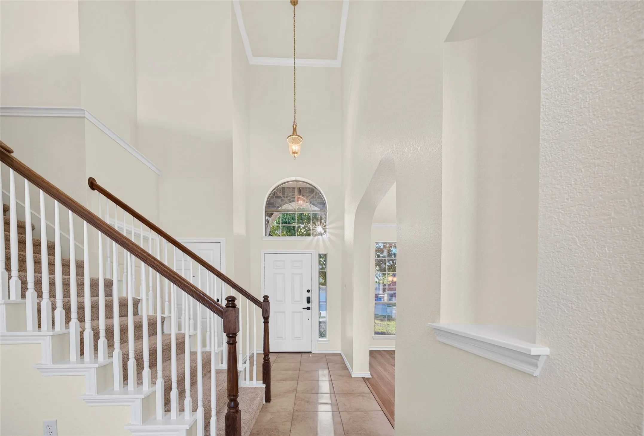 Two-story entryway featuring a decorative light fixture, tiled flooring, wood banister staircase, and an arched transom window above the front door