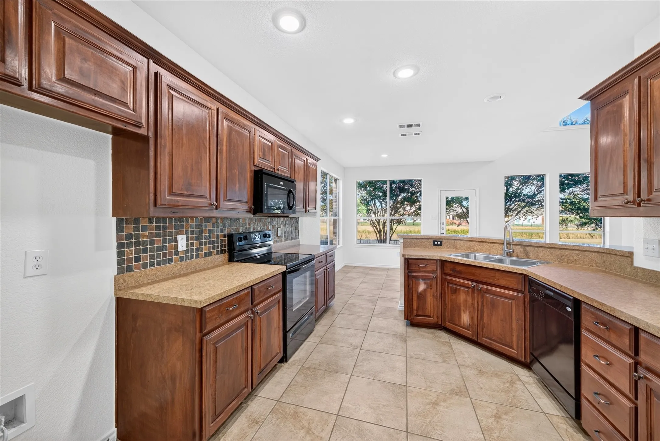 Expansive kitchen with abundant wood cabinetry, tiled flooring, integrated stainless steel sink, and multiple windows