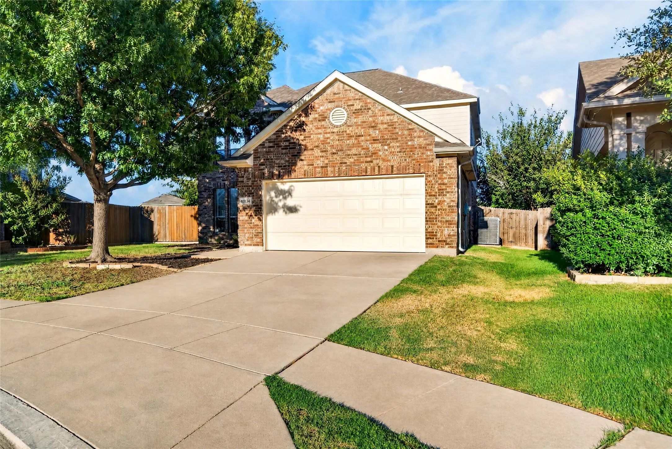 Brick and siding exterior with an attached garage, concrete driveway, and mature front yard tree
