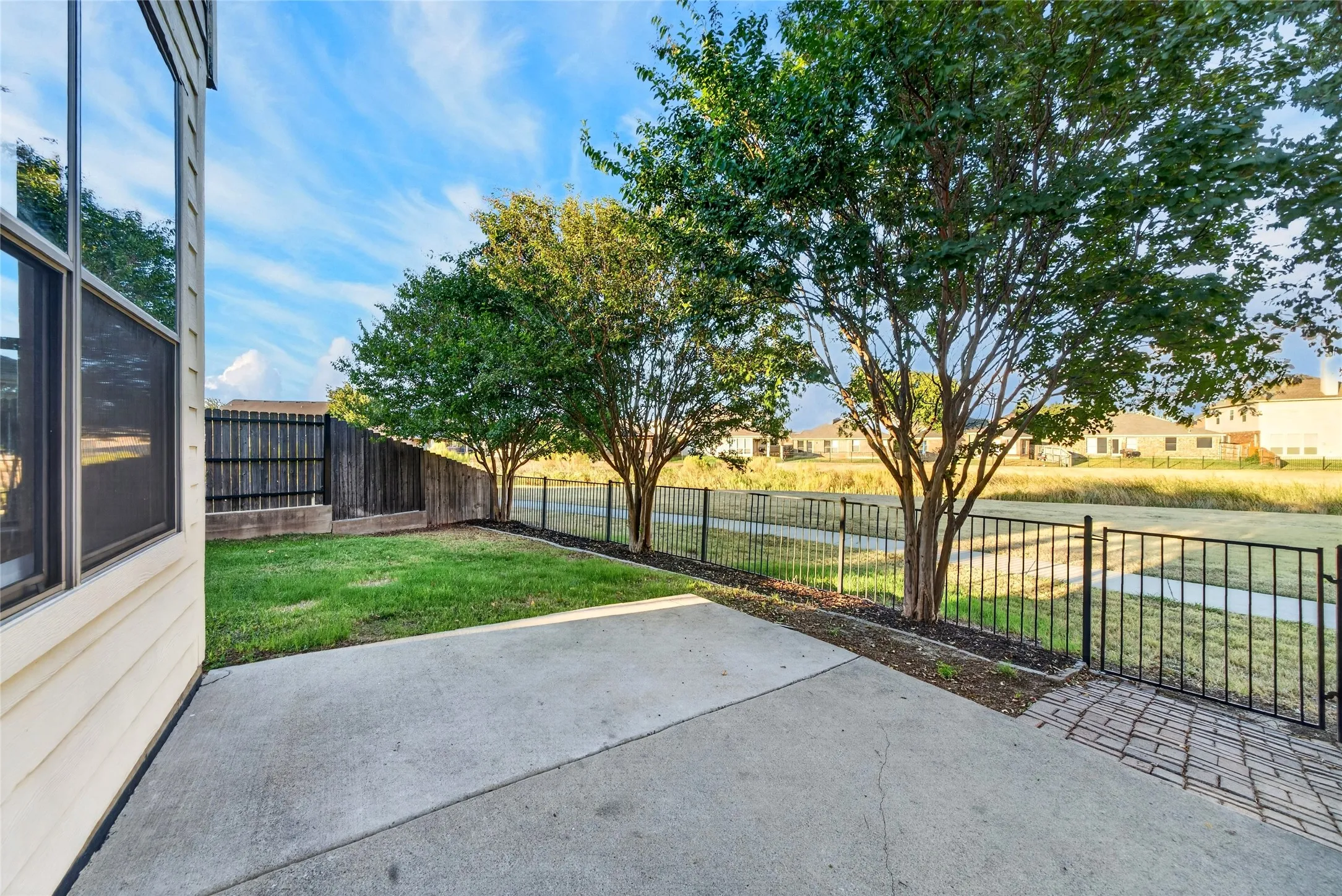 Expansive concrete patio with a brick paver accent, bordered by a wrought iron fence