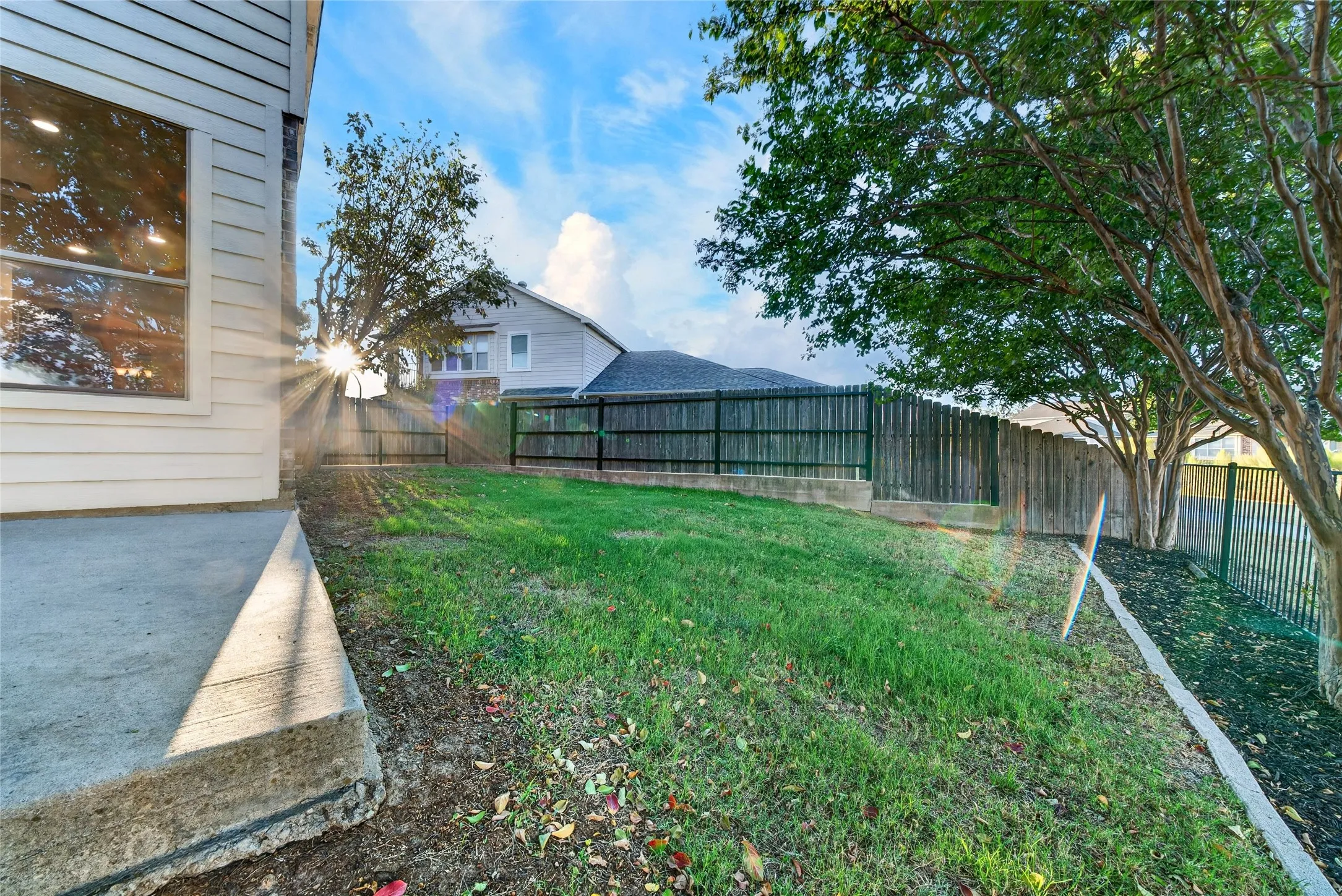 Rear exterior showcasing a concrete patio, wood fence, and mature trees