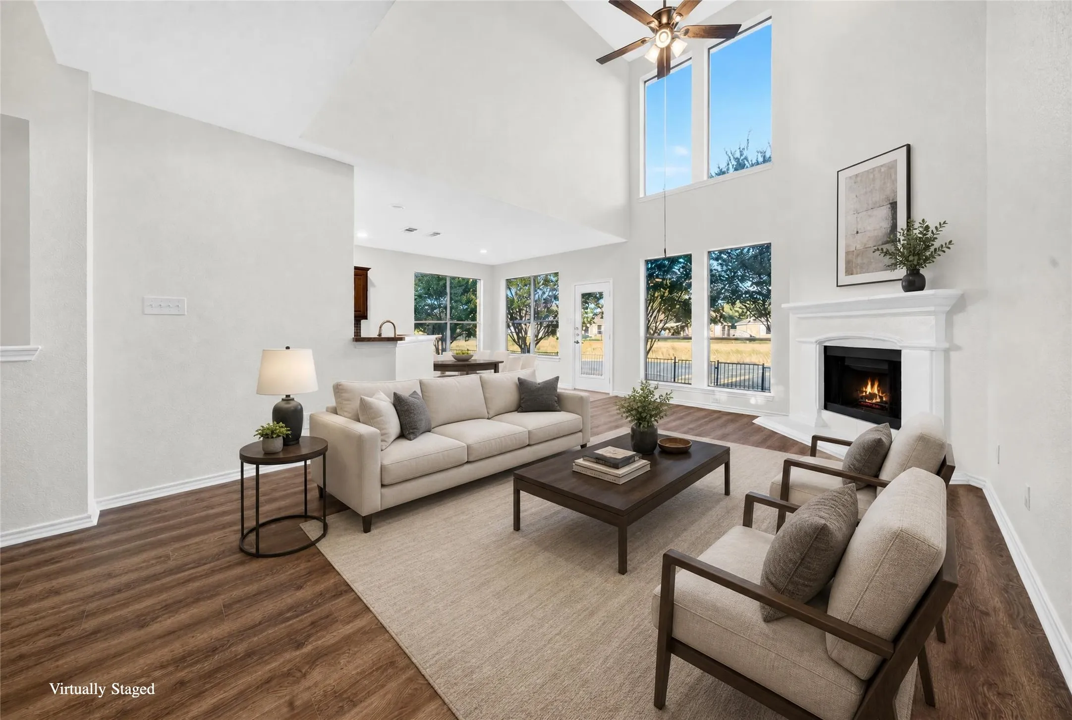 Vaulted ceiling with a ceiling fan, fireplace with a white mantel, wood-finish flooring, and multiple large windows