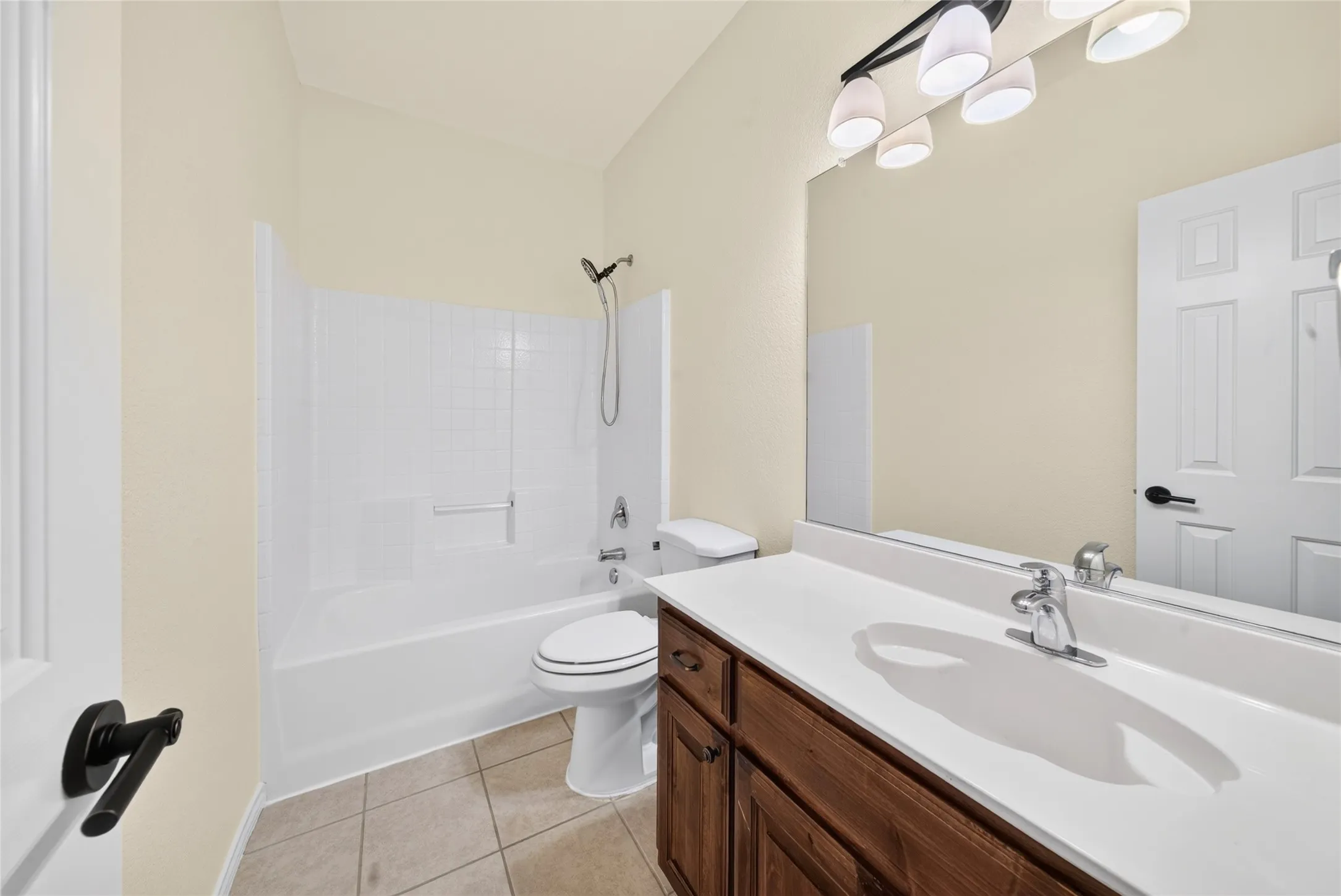 Bathroom featuring a white tub/shower combination, a vanity with a white countertop and wood-finish cabinetry, a large wall-mounted mirror, and tile flooring