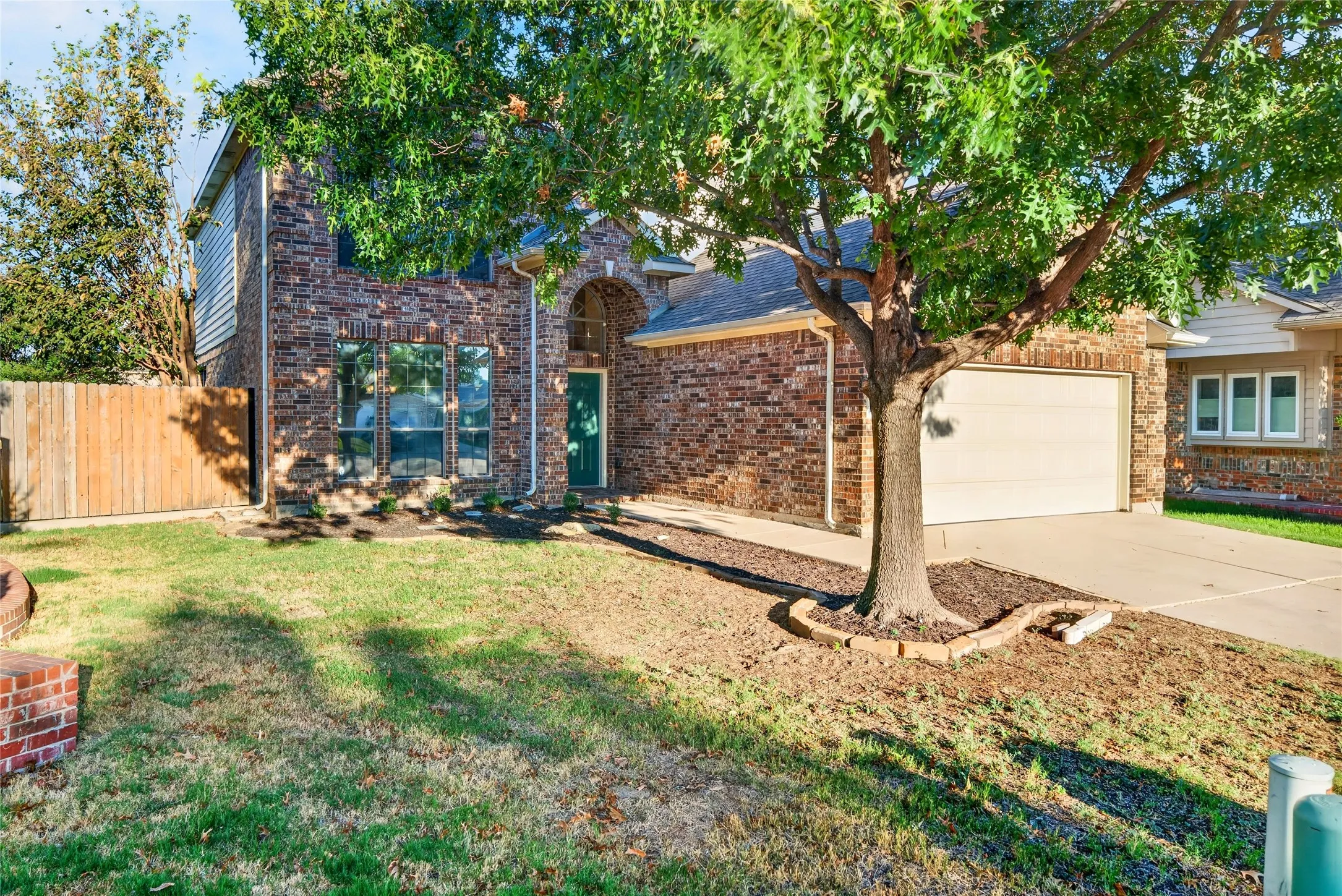 Brick exterior with arched entry, attached garage, and mature tree