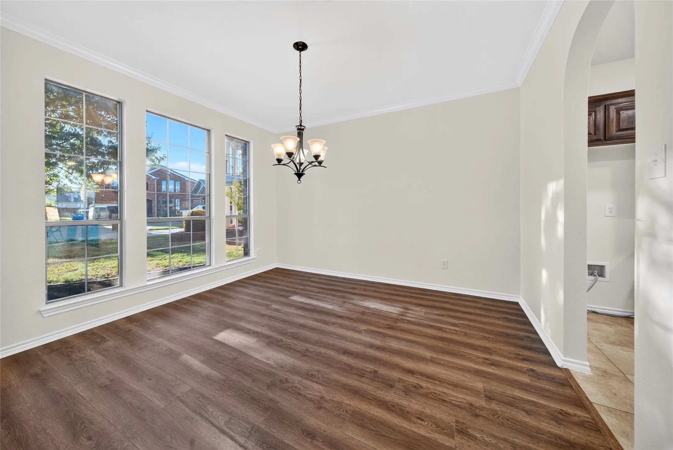 Wood-finish flooring, crown molding, a decorative chandelier, and large windows with grid accents