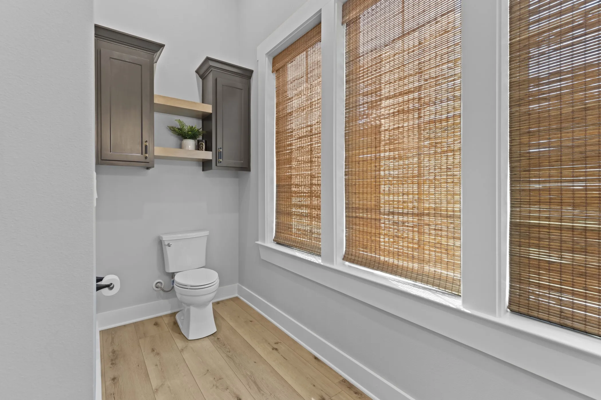 Powder room featuring wood-finish flooring, three windows with woven blinds, and built-in cabinetry with open shelving