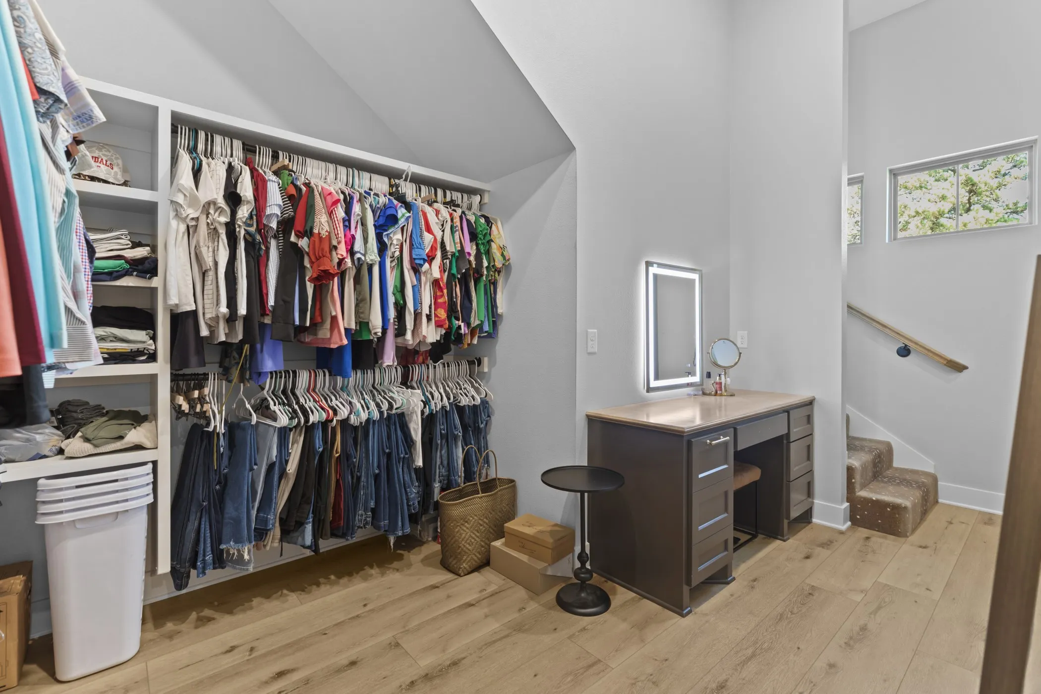 Custom closet organization system, wood-finish flooring, built-in vanity with illuminated mirror, light wood handrail, and carpeted stairs