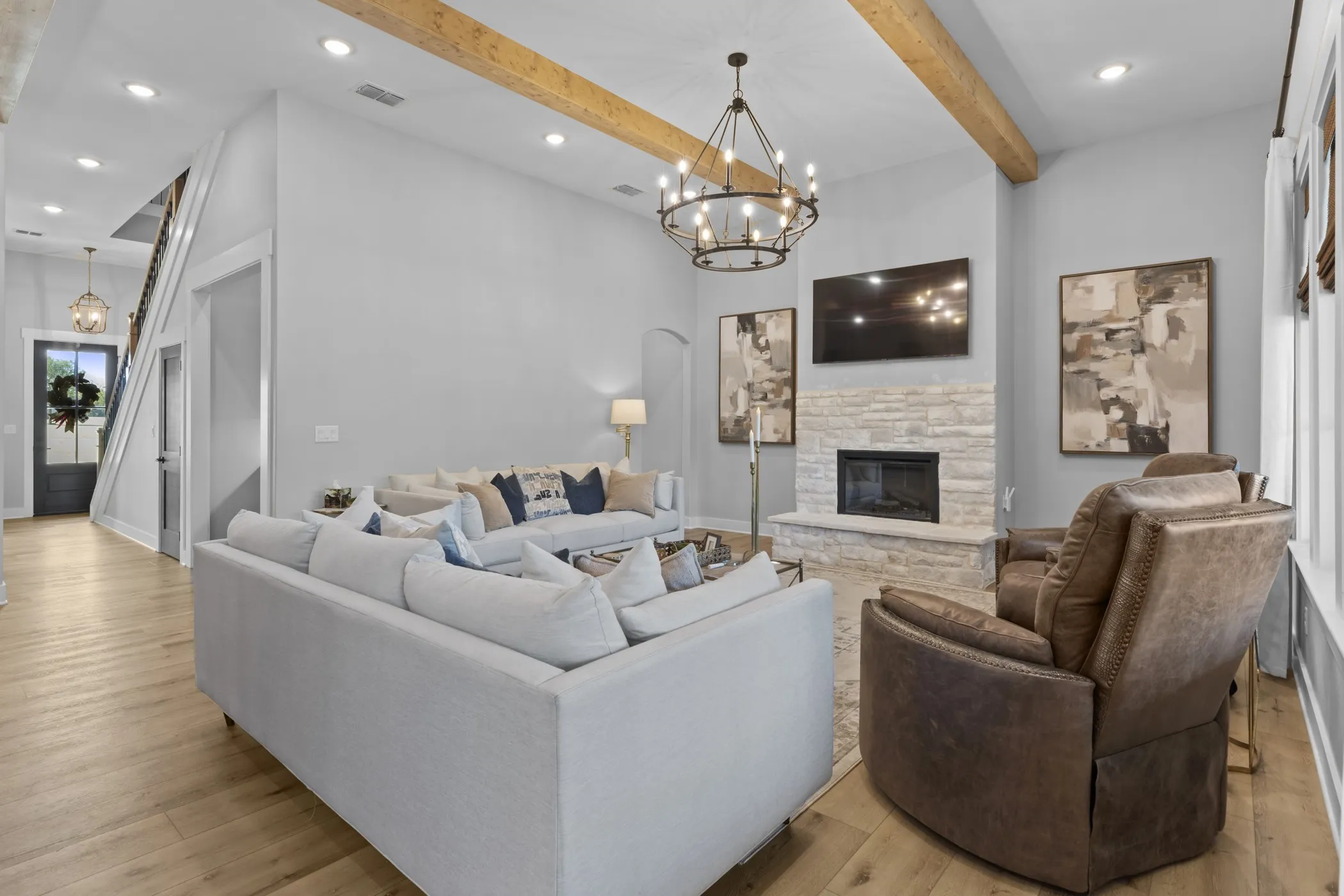 Vaulted ceiling with exposed wood beams, stone-faced fireplace, wood-finish flooring, and a wrought iron​​‌​​​​‌​​‌‌​‌‌​​​‌‌​‌​‌​‌​​​‌​​ chandelier