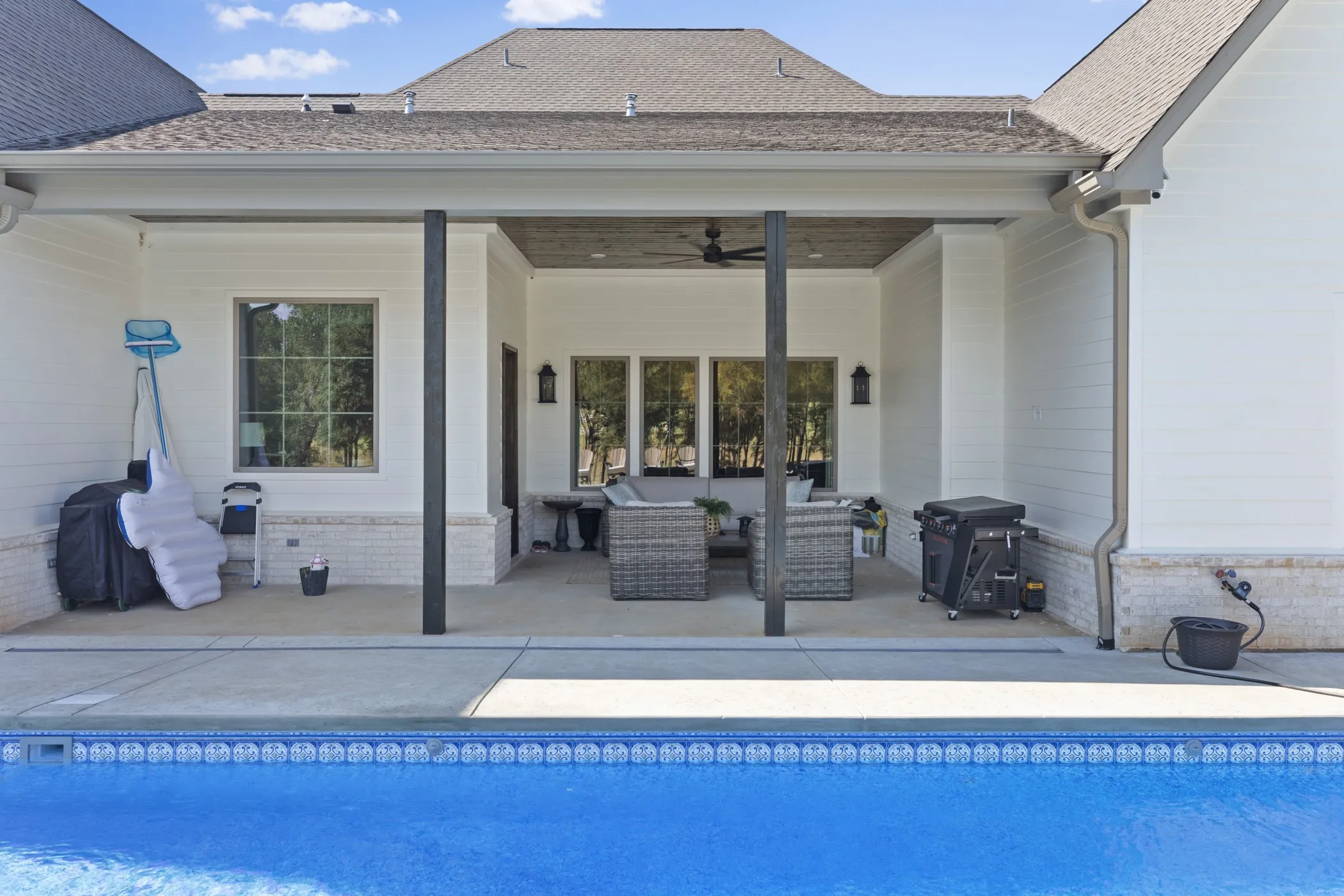 Outdoor concrete patio with recessed lighting and a ceiling fan, featuring an adjacent swimming pool with a tiled edge