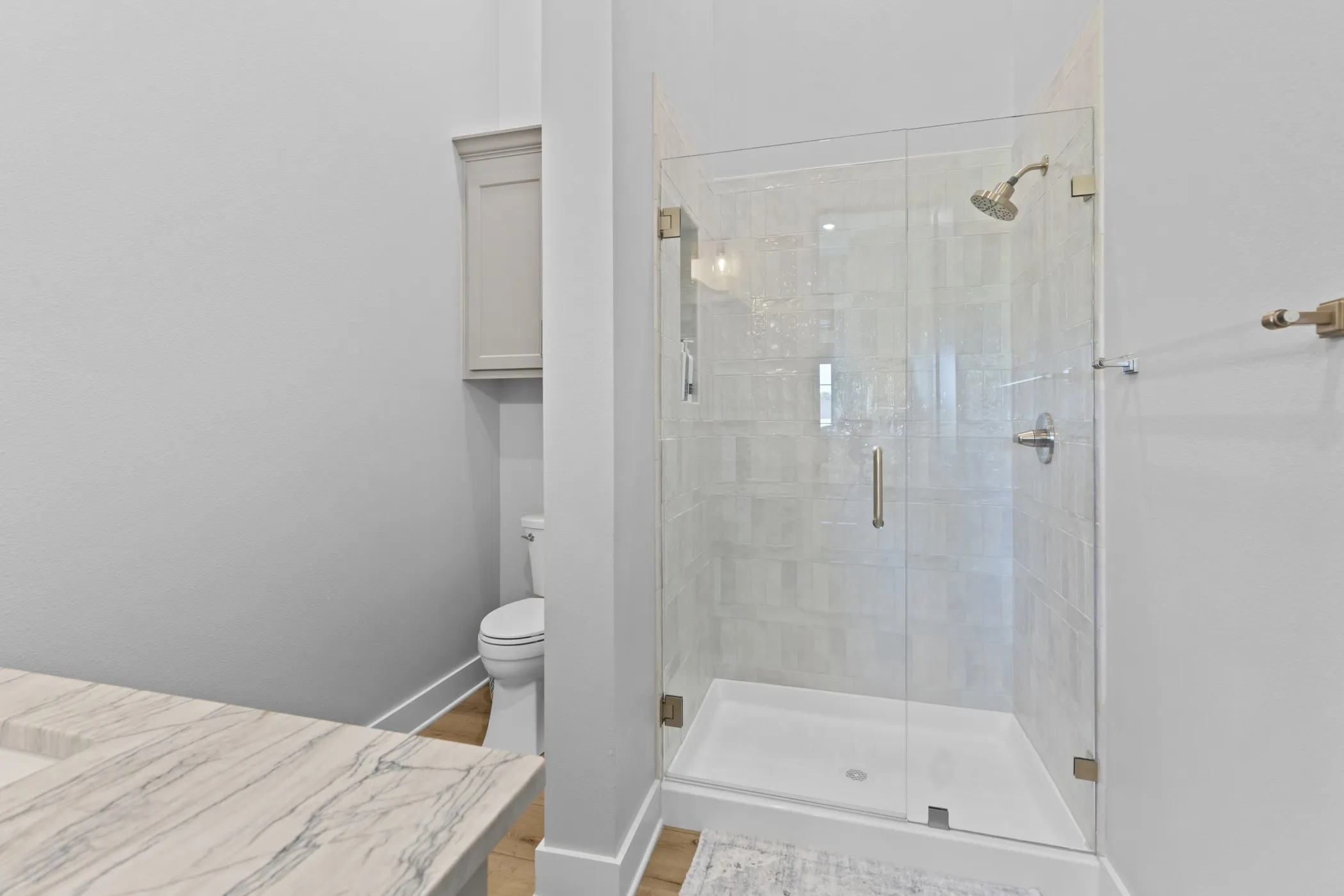Glass-enclosed shower with a tiled surround, built-in toilet, stone-finish countertop, and wood-finish flooring