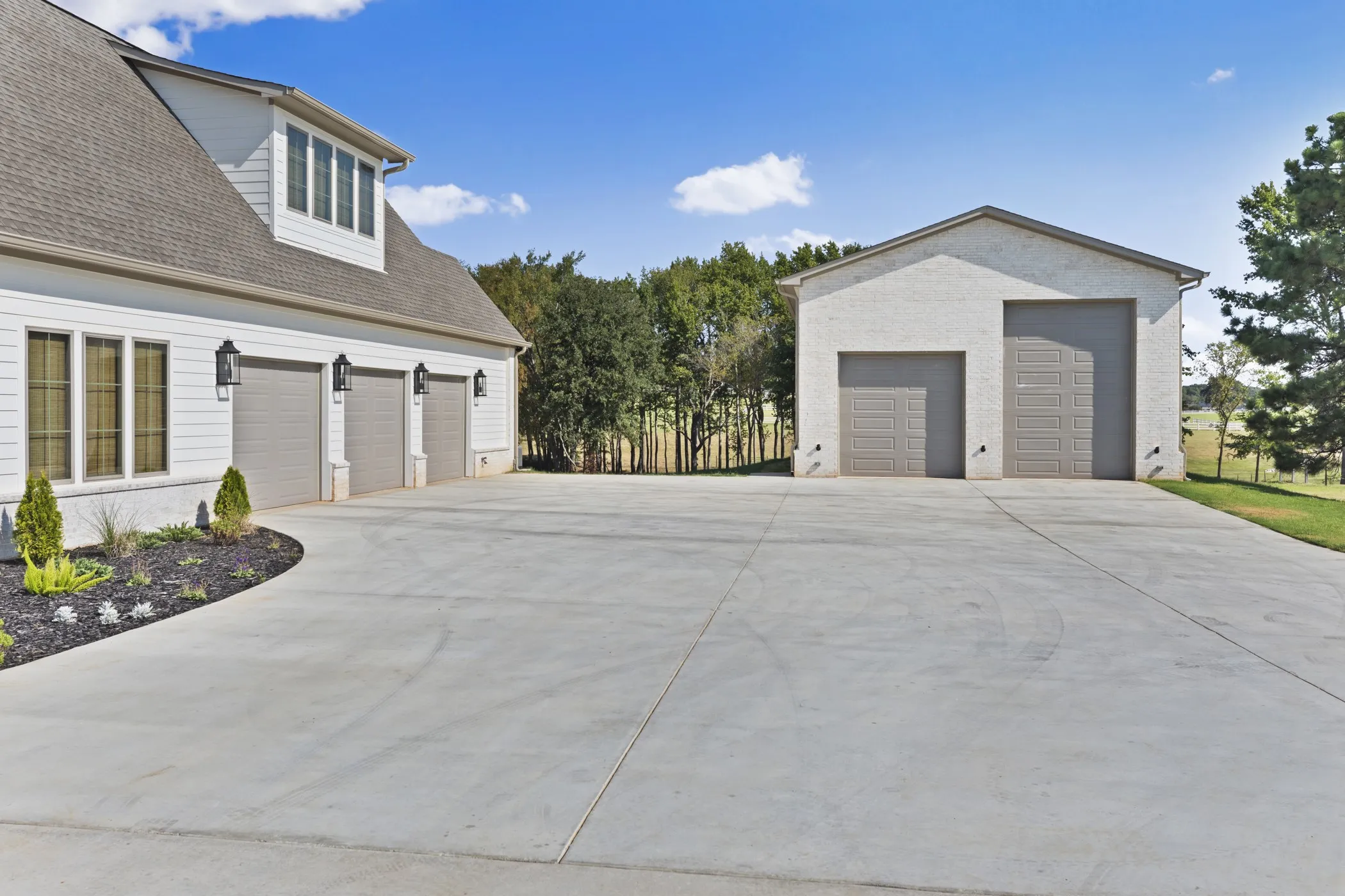Three-car attached garage with white siding, dormer windows, and black exterior lighting