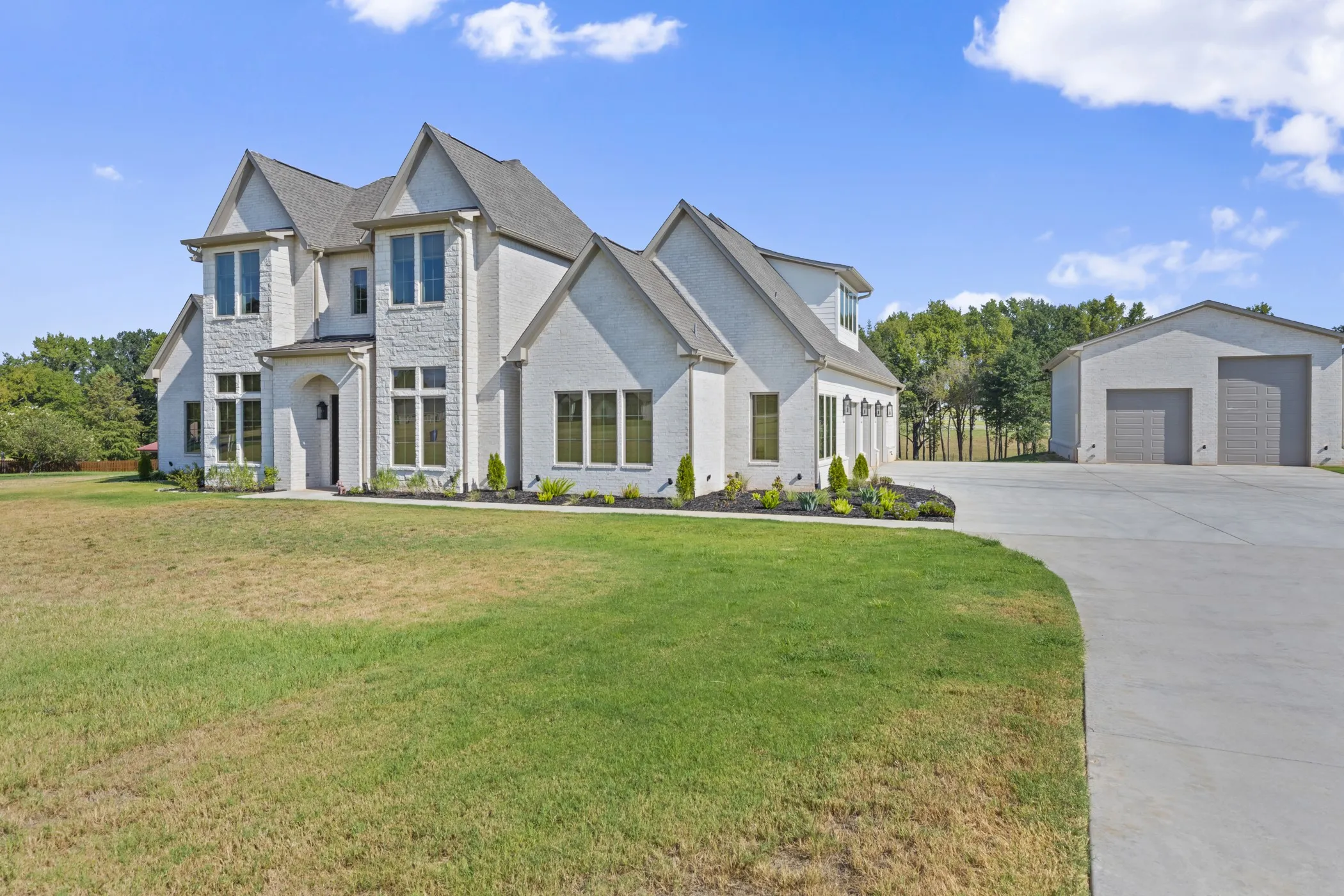 Stately residence featuring a light-colored brick and stone exterior, multiple gables, a covered entry, and a dedicated detached garage structure