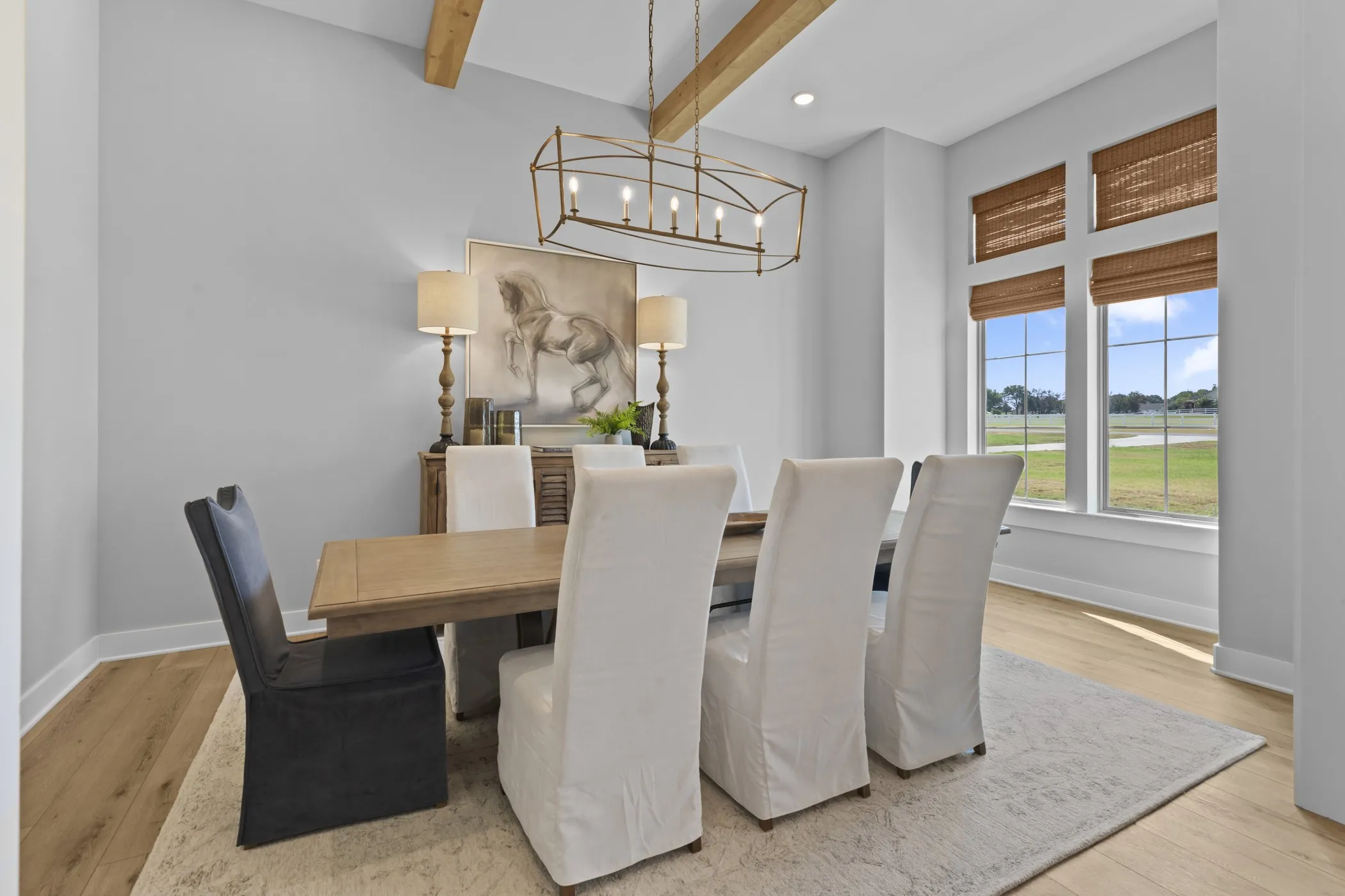 Vaulted ceiling with exposed wood beams, wood-finish flooring, large windows with natural light, modern chandelier, and built-in buffet