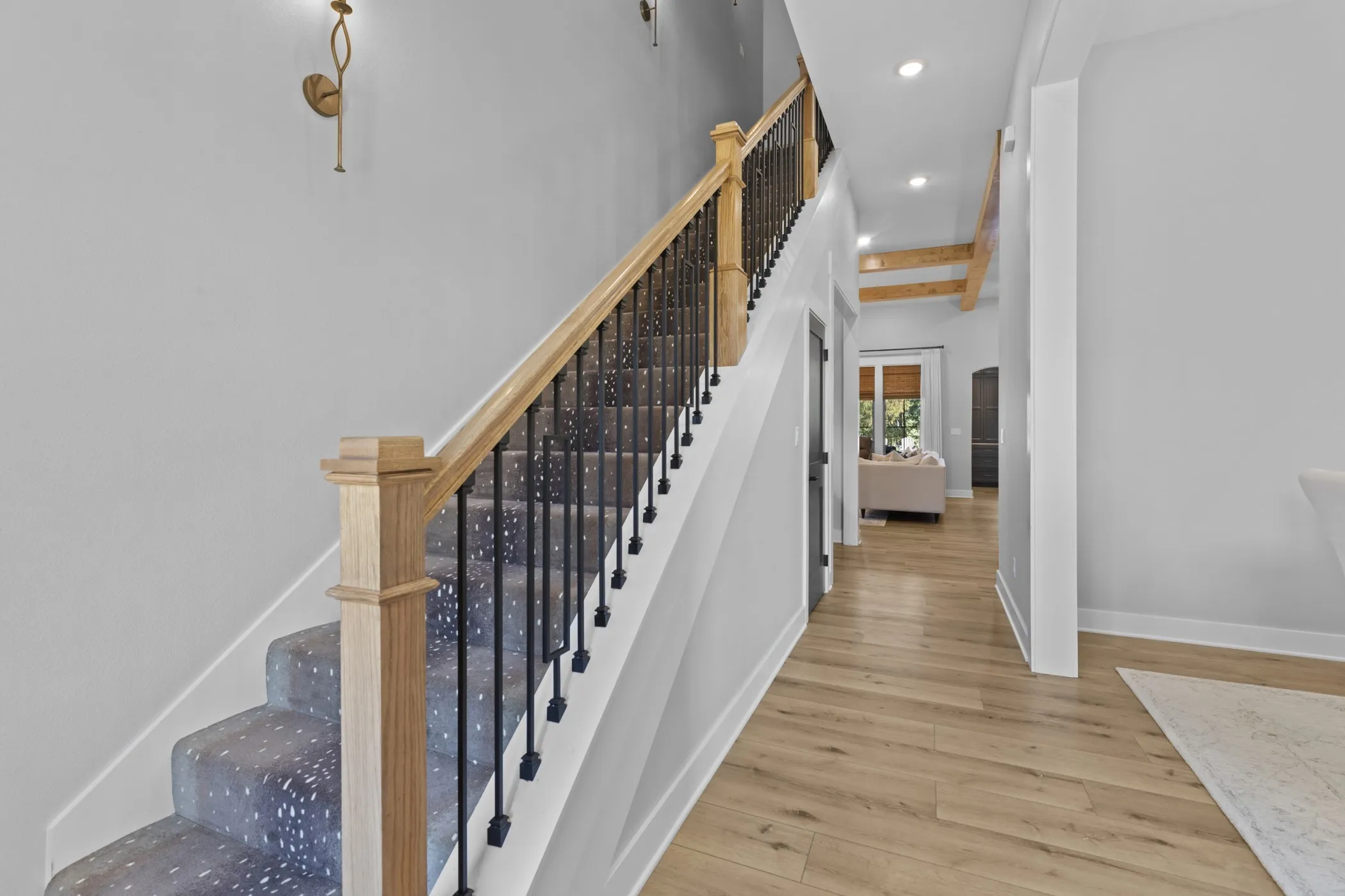 Staircase with wood newel post and handrail, black wrought iron balusters, and patterned carpet runner