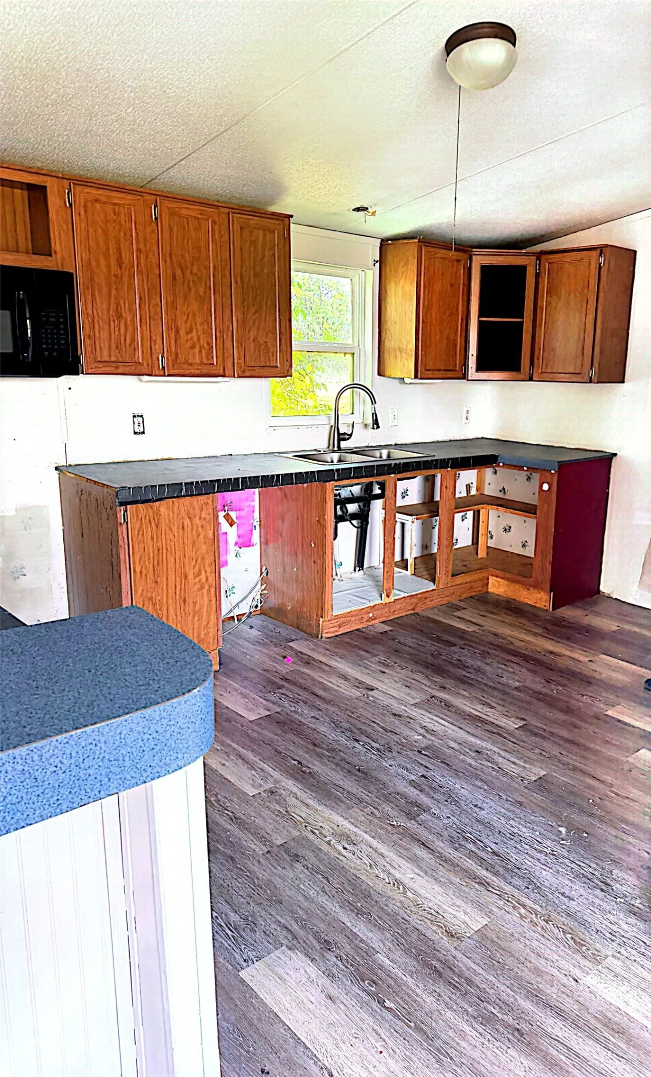 Wood-finish flooring, wood cabinetry, and a stainless steel sink with a gooseneck faucet