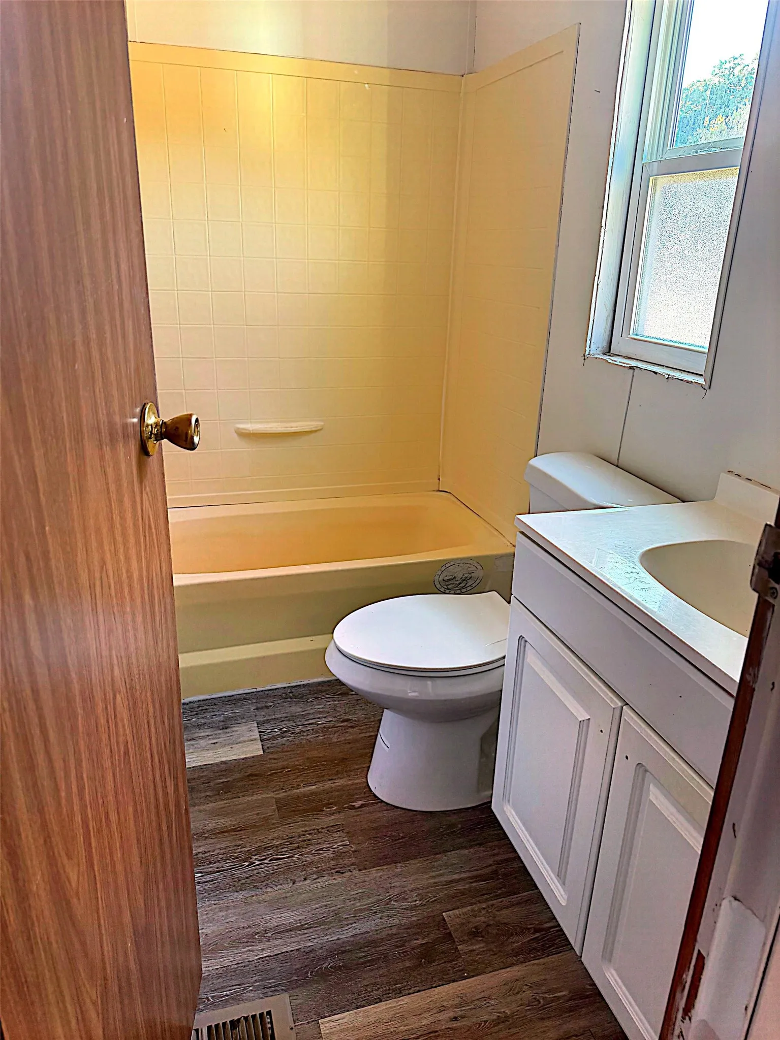 Tub/shower combination with a textured surround, wood-finish flooring, and a white vanity with an integrated sink