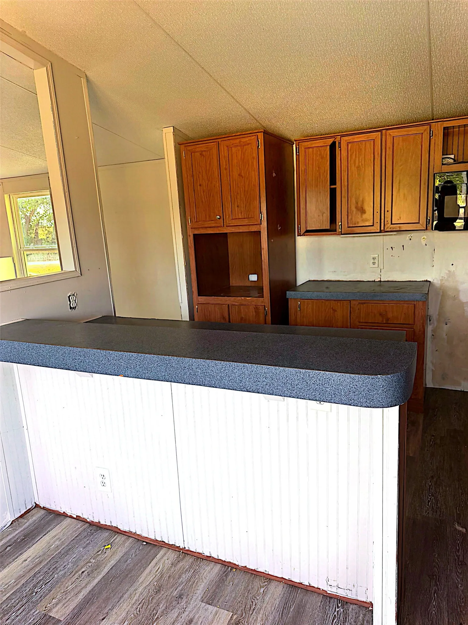 Wood-finish flooring, white beadboard paneling, L-shaped breakfast bar, laminate countertops, and wood cabinetry