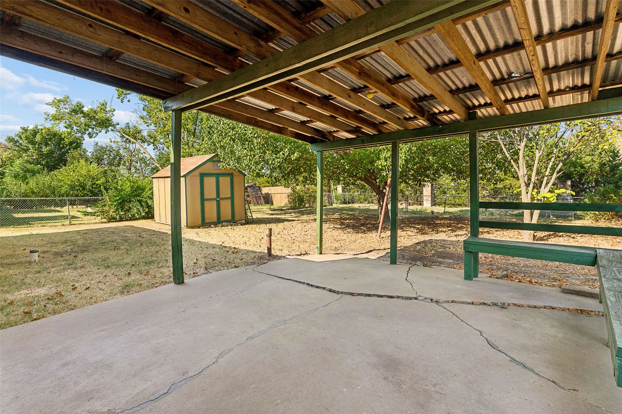 Covered patio with exposed wood beams, corrugated metal roof, built-in wooden seating, and a detached storage shed