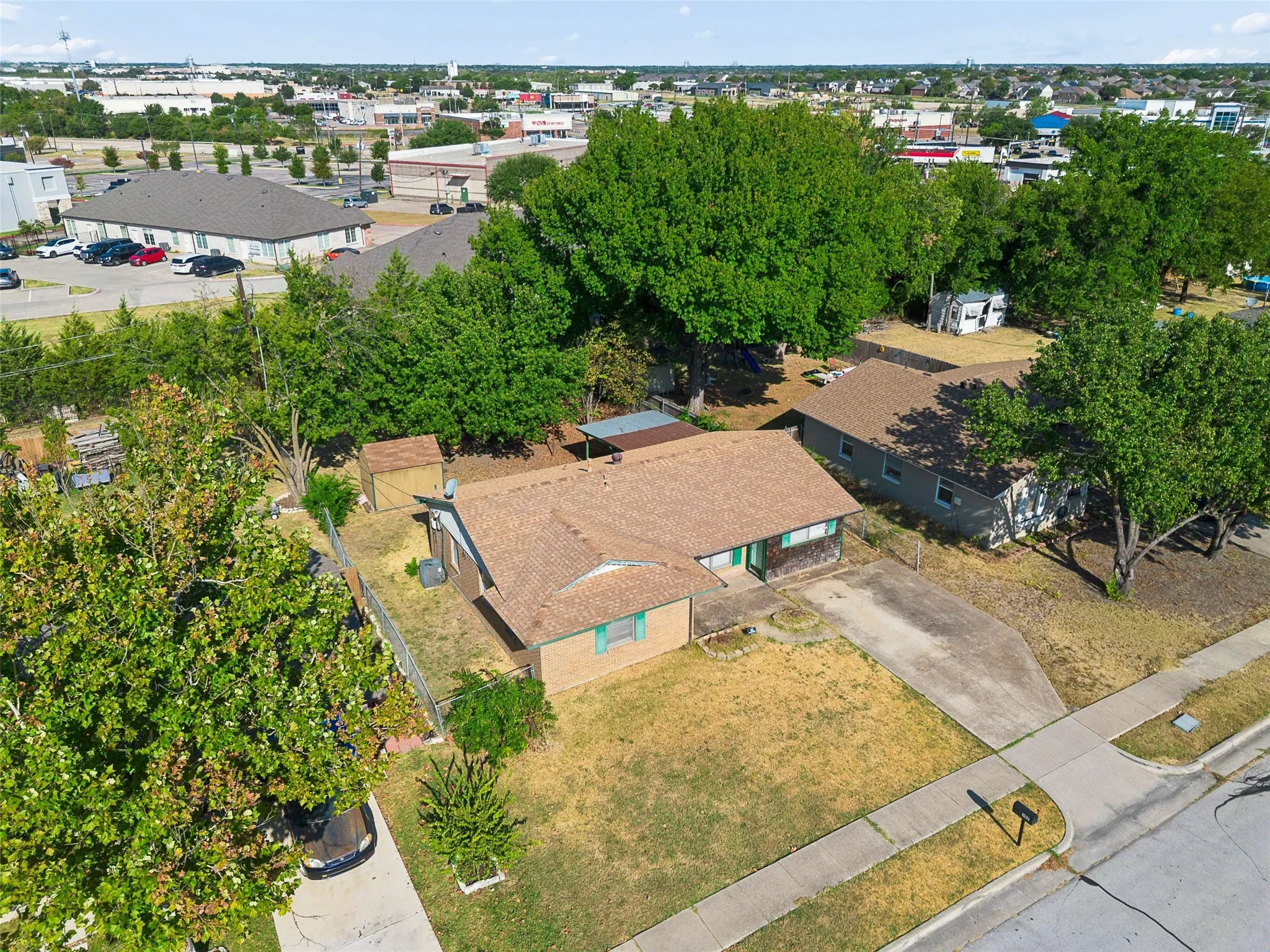Brick exterior with green trim, fenced backyard, detached storage shed, and mature trees