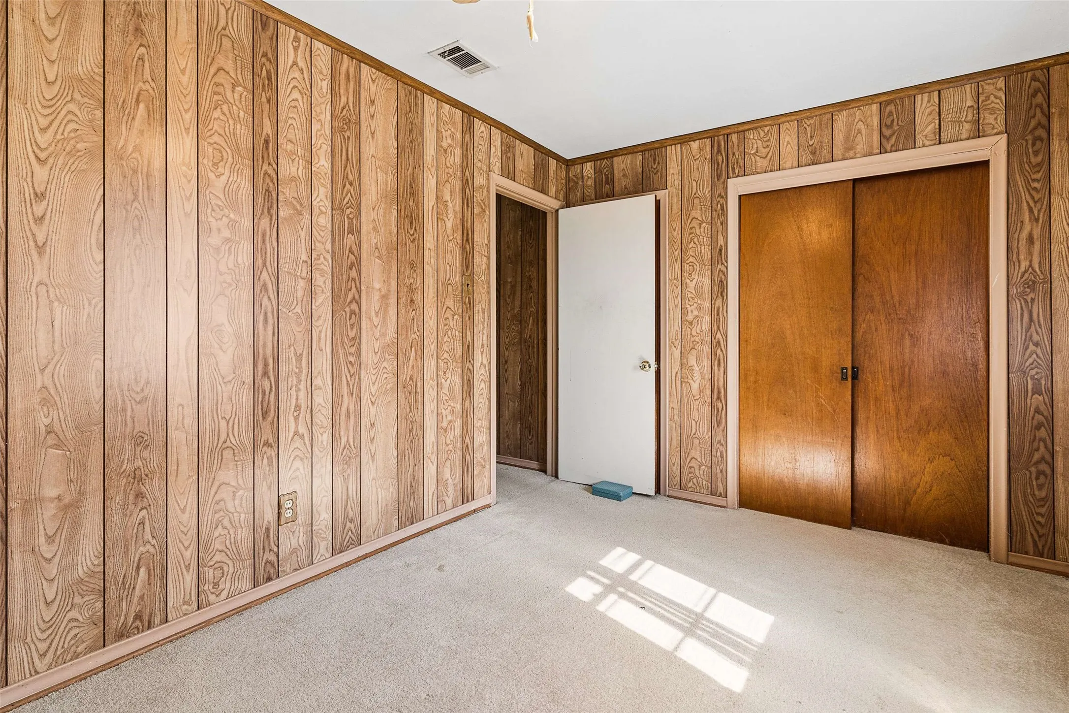 Vertical wood paneling, light-toned carpeting, wood-finish trim, and a built-in closet with bi-fold doors
