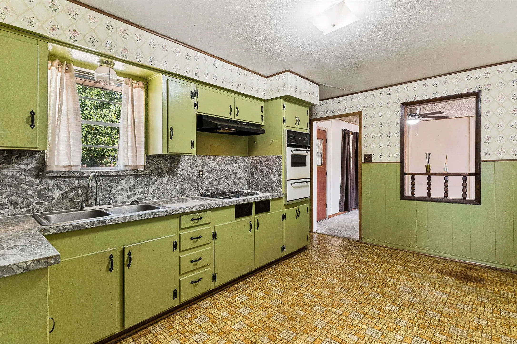 Kitchen featuring ample cabinetry, dual basin stainless steel sink, built-in wall oven, and a pass-through window