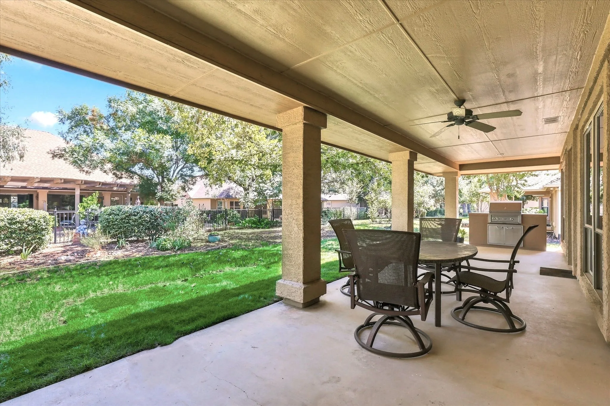 Covered patio with a ceiling fan, concrete flooring, and built-in outdoor cooking station. Green lawn has been virtually enhanced.