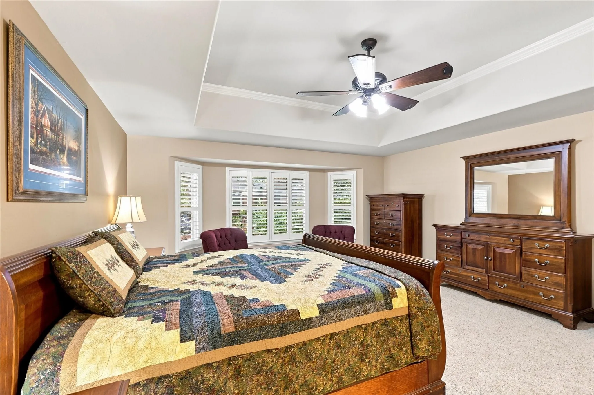 Tray ceiling with crown molding, ceiling fan, and bay window featuring plantation shutters