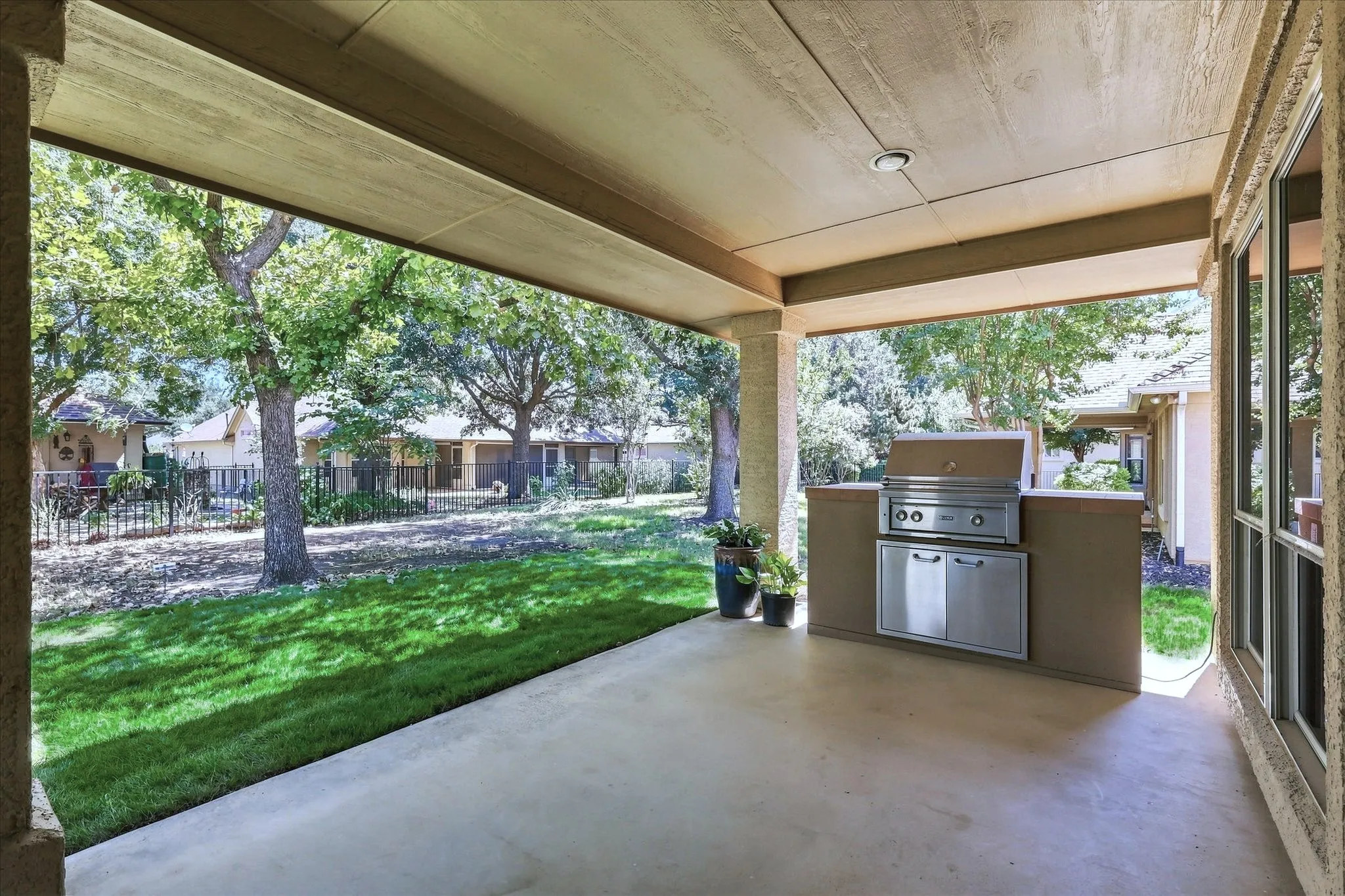 Covered patio with an integrated outdoor grill, recessed lighting, and expansive concrete flooring. Green lawn has been virtually enhanced.