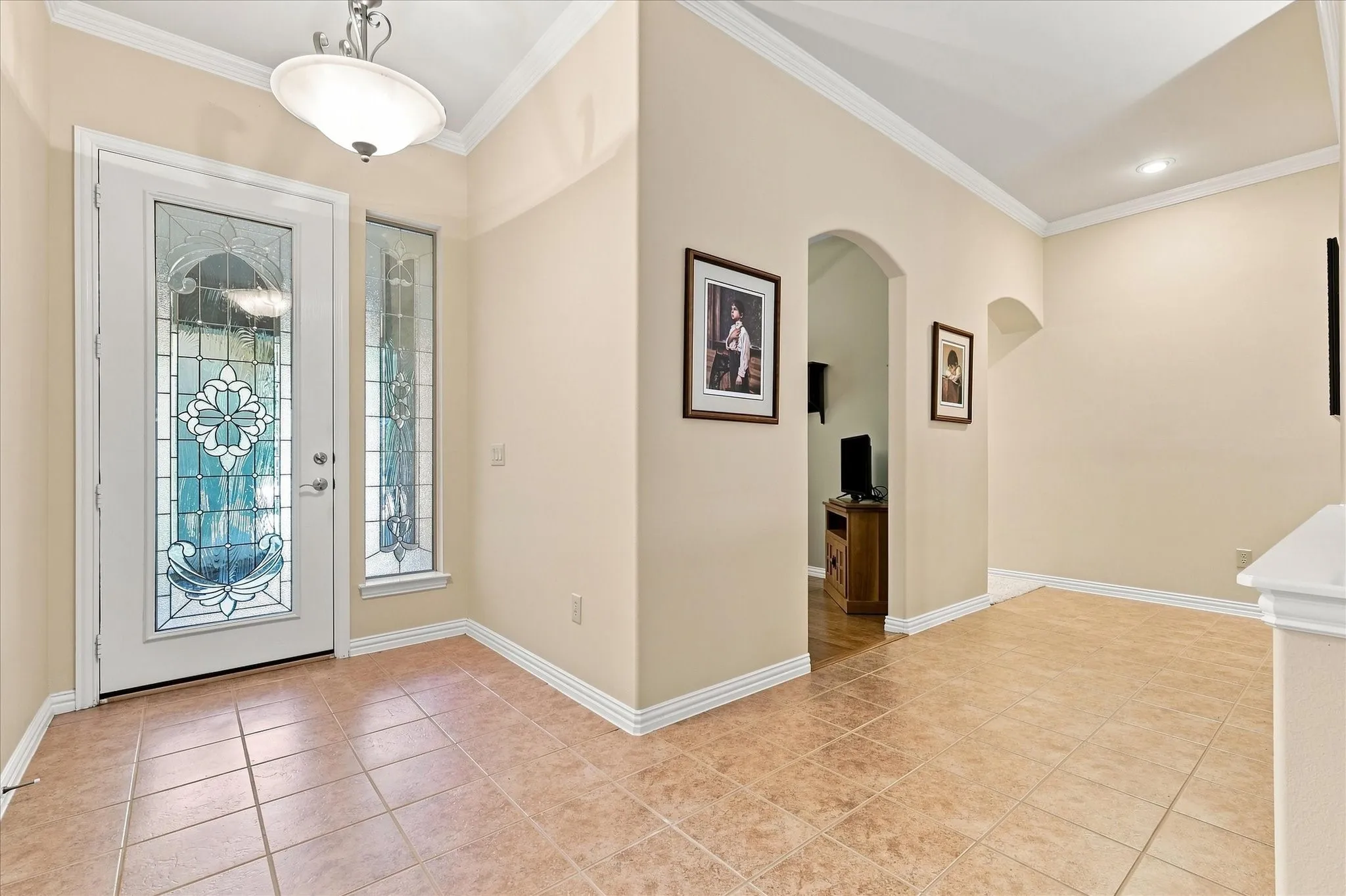 Entryway featuring a decorative glass paneled door, coordinating sidelight, tiled flooring, crown molding, and an arched doorway