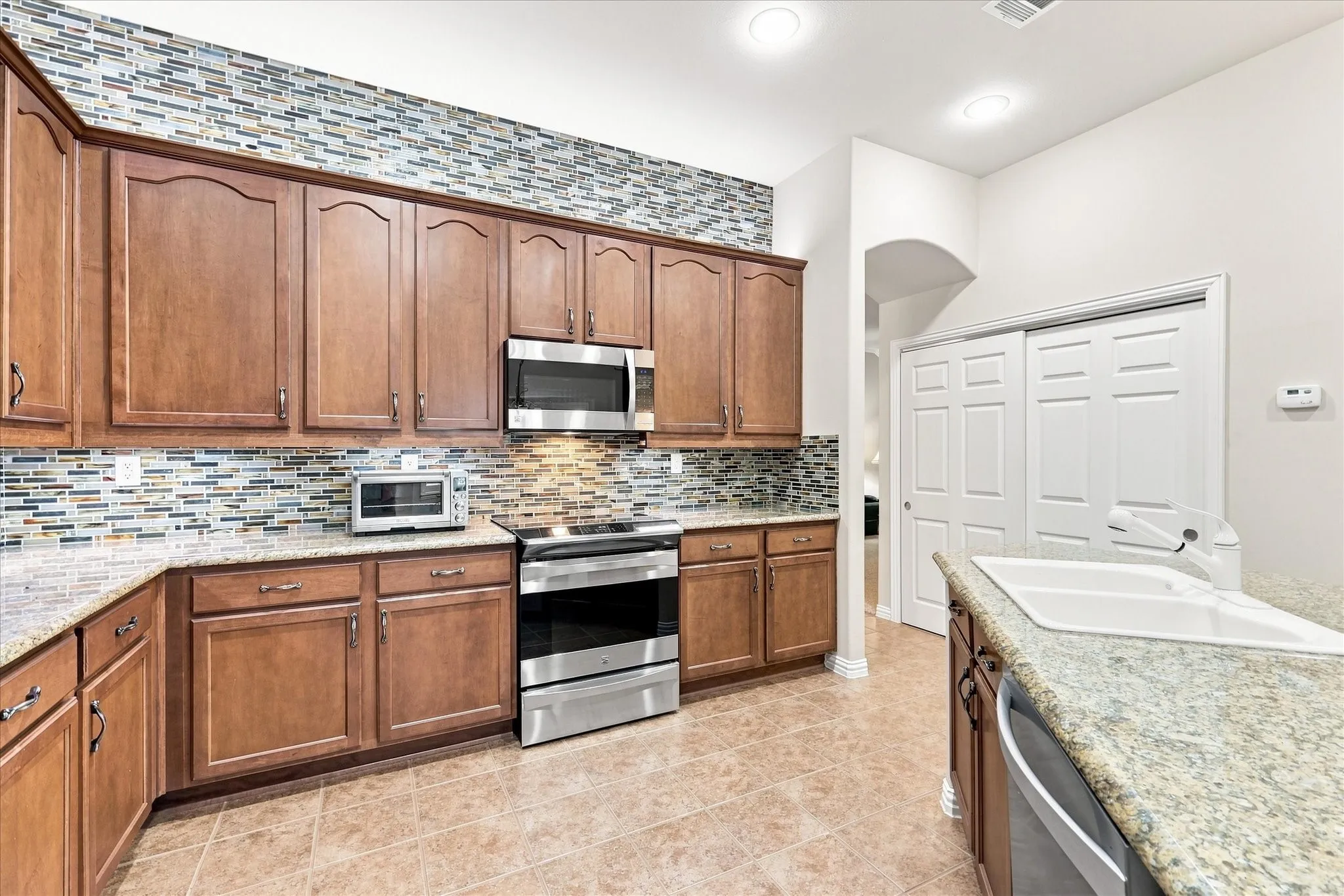 Kitchen featuring wood cabinetry, stainless steel appliances, granite countertops, a tiled backsplash, and tile flooring