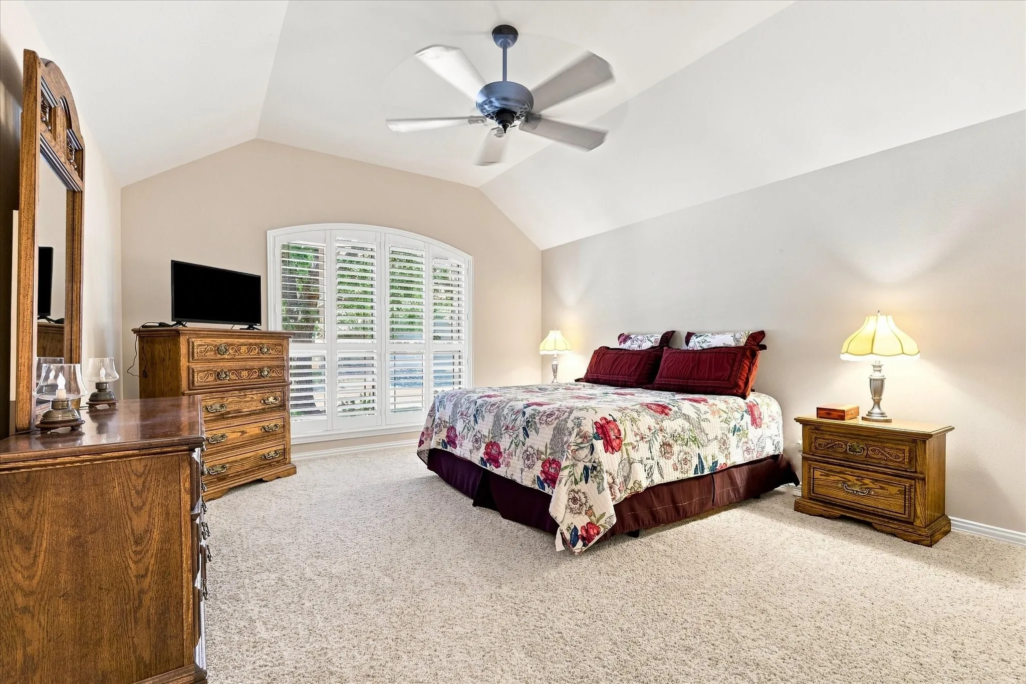 Vaulted ceiling with a ceiling fan, arched window with plantation shutters, and light-toned carpeting