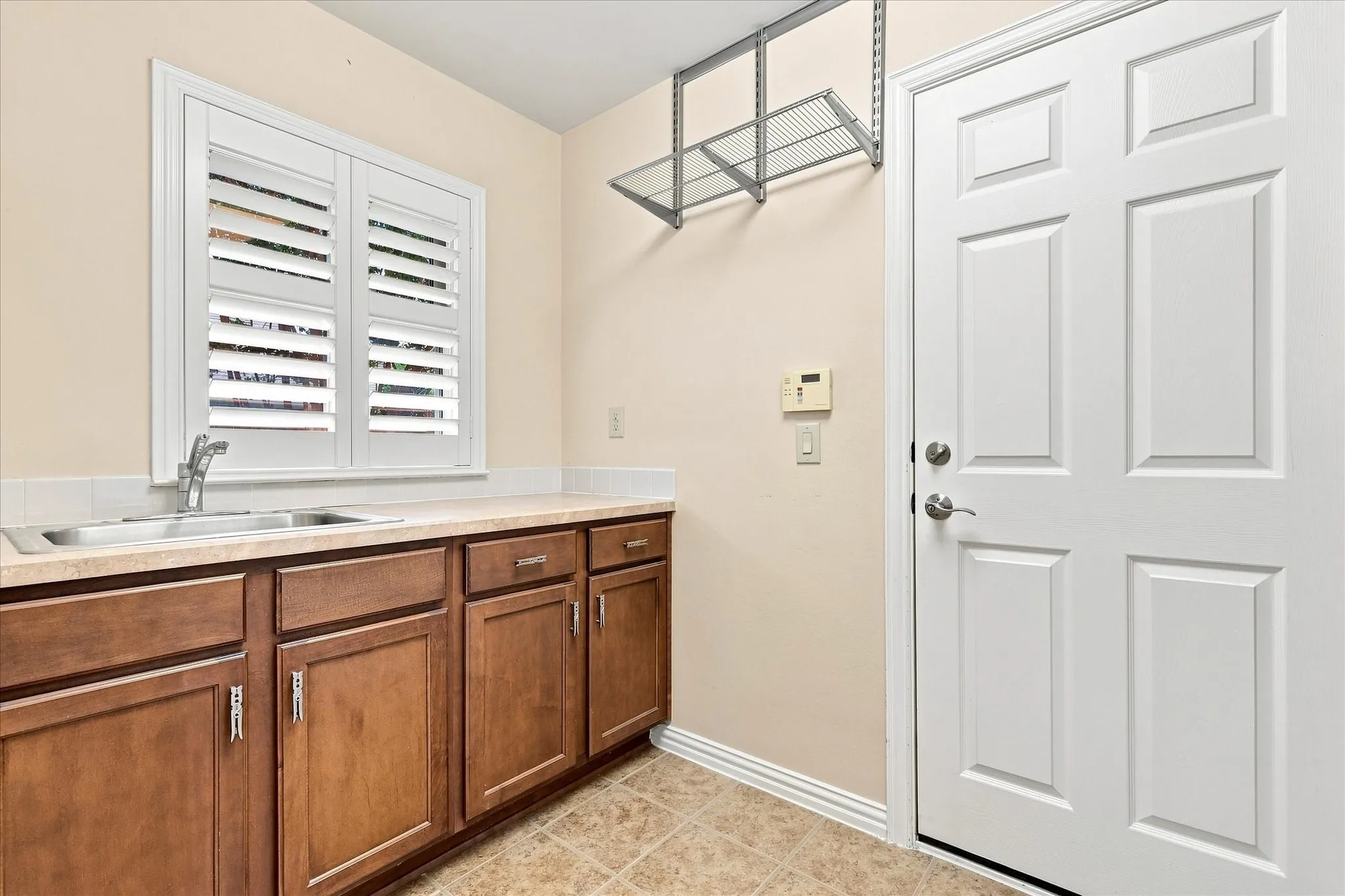 Built-in stainless steel sink, wood cabinetry, white plantation shutters, and tiled flooring