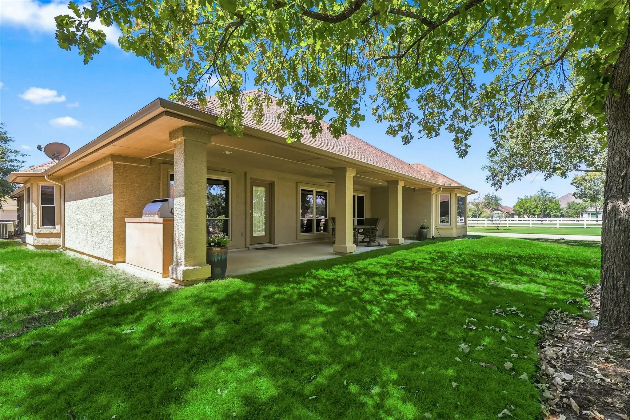 Expansive covered patio with columns, multiple exterior entry points, and an integrated outdoor grilling station. Green lawn has been virtually enhanced.