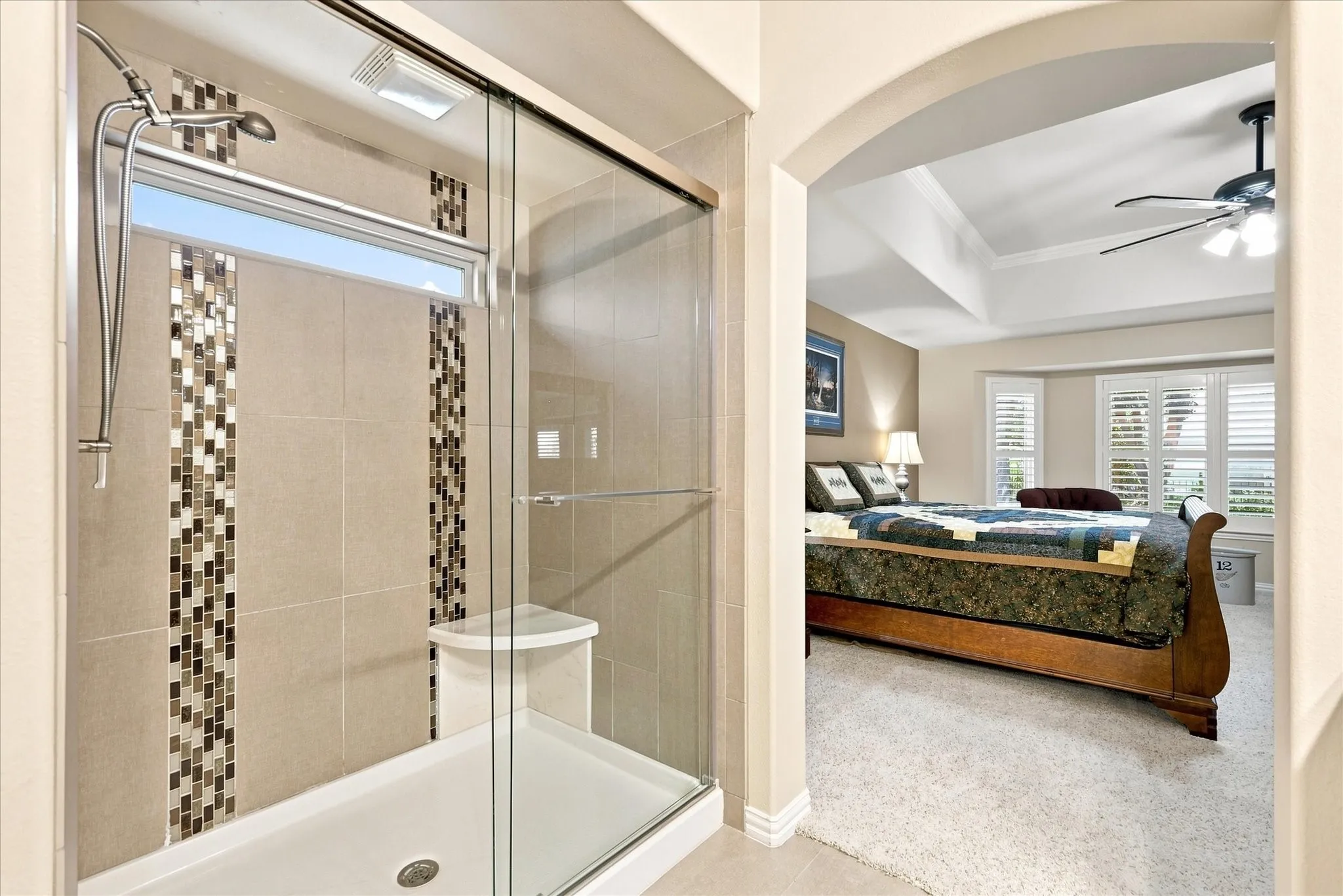 Glass-enclosed shower with tiled walls, decorative mosaic accents, and a built-in corner bench