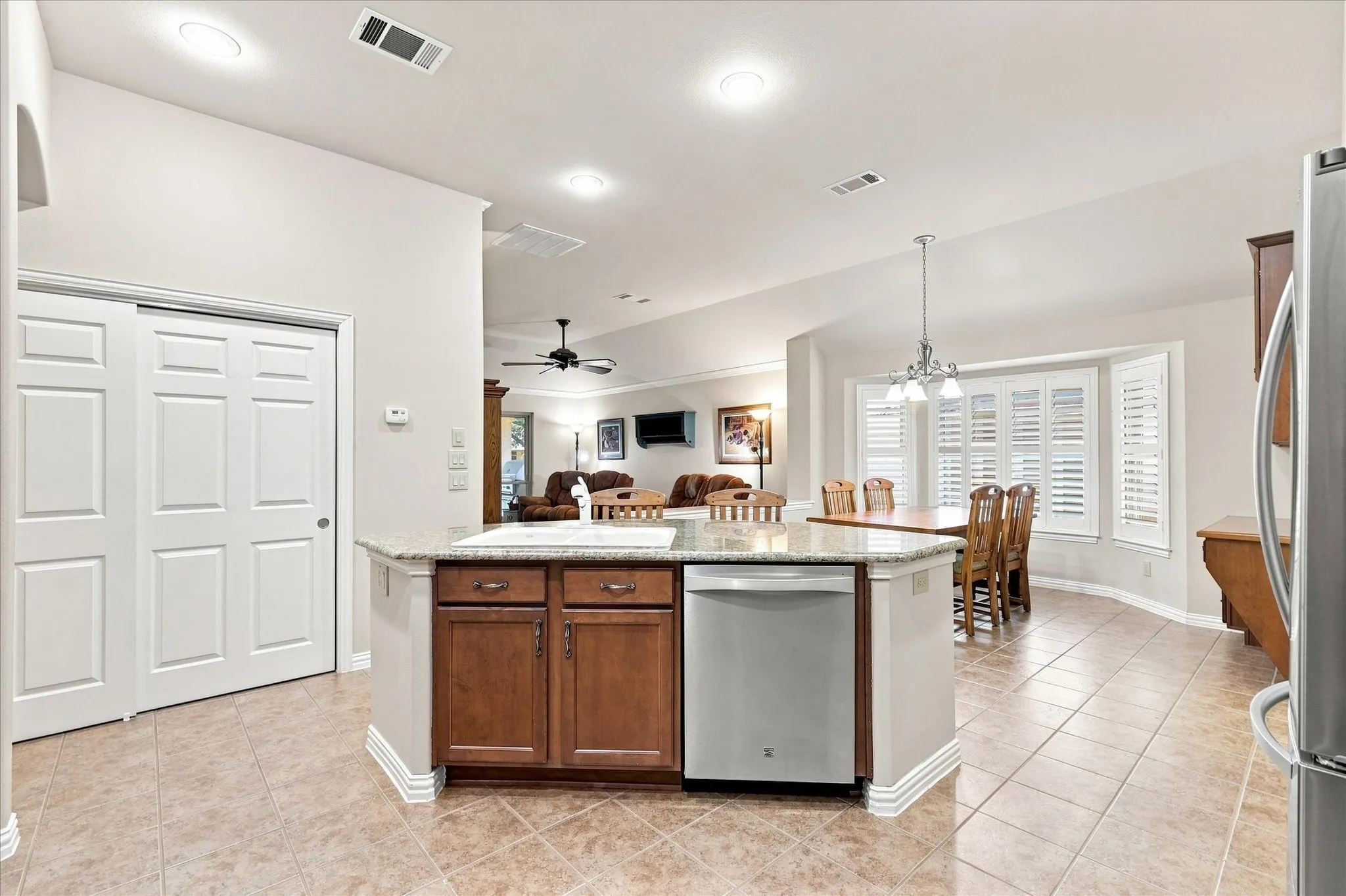 Open-concept kitchen with ceramic tile flooring, a center island featuring a built-in sink and dishwasher, and wood cabinetry