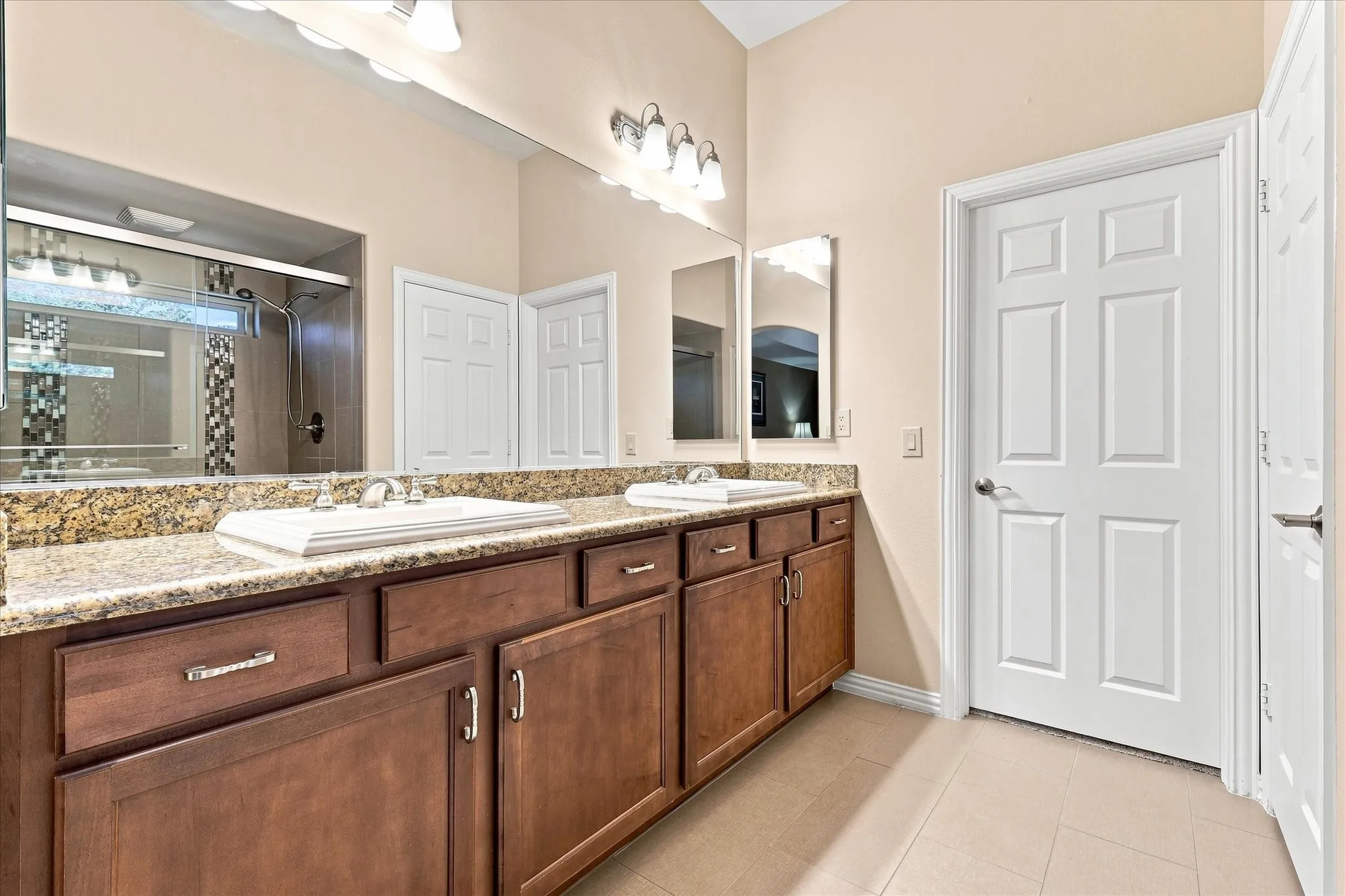 Dual vanity with  granite countertop, wood-finish cabinetry, medicine cabinets, updated shower