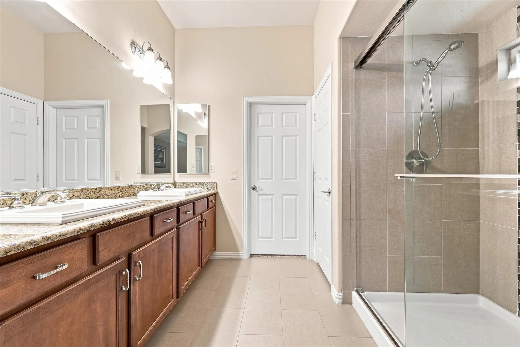 Dual sink vanity with wood-finish cabinetry, granite countertop, and a large wall-mounted mirror