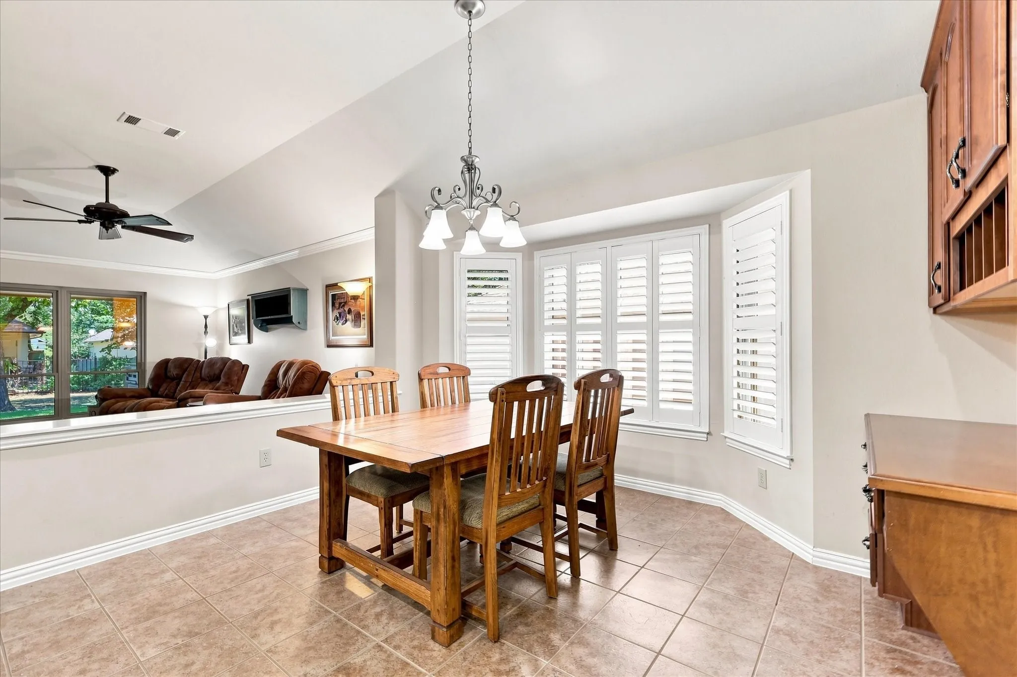 Bay window with white plantation shutters, tile flooring, vaulted ceiling
