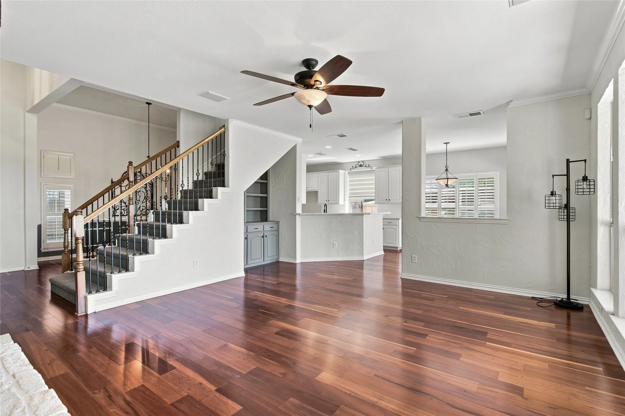 Living room and staircase with wrought iron balusters, built-in cabinetry, and ceiling fan