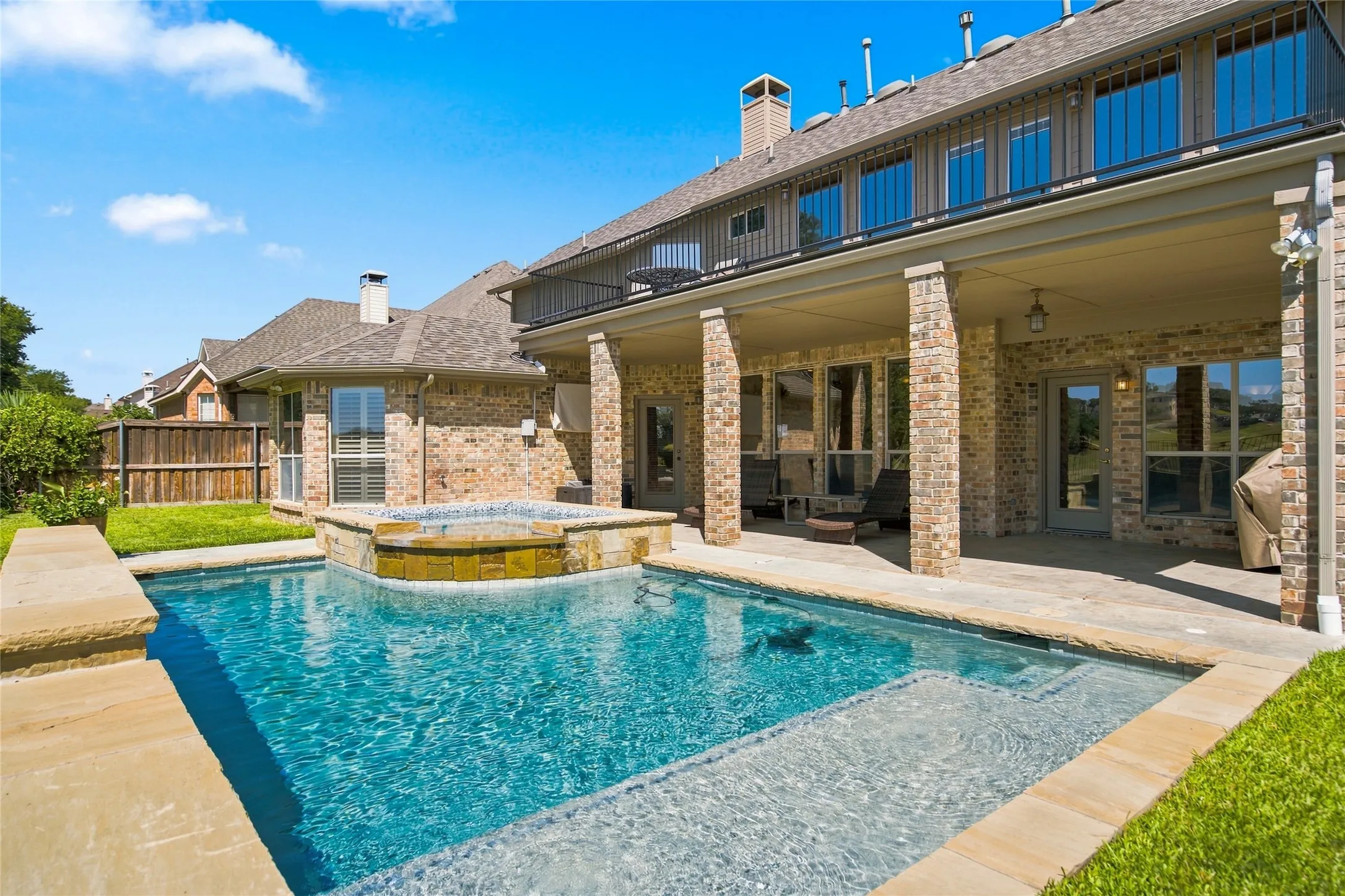 Brick exterior with a covered patio, featuring a built-in pool and integrated spa.